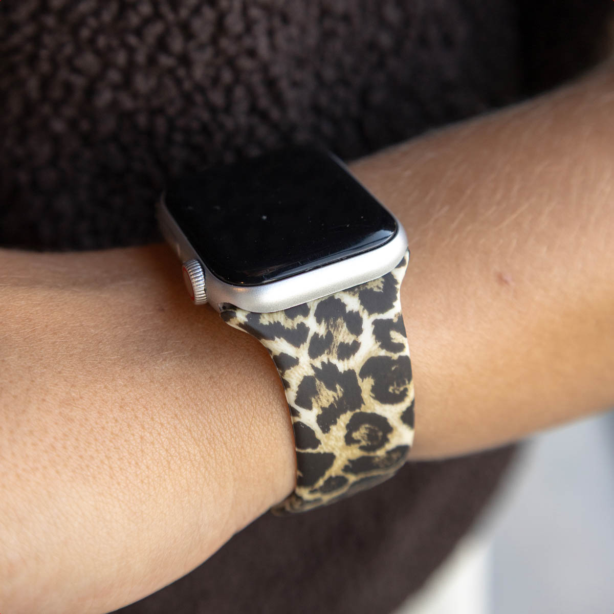 A person's arm wearing an Apple Watch with a leopard print strap. The watch has a black screen and silver casing.