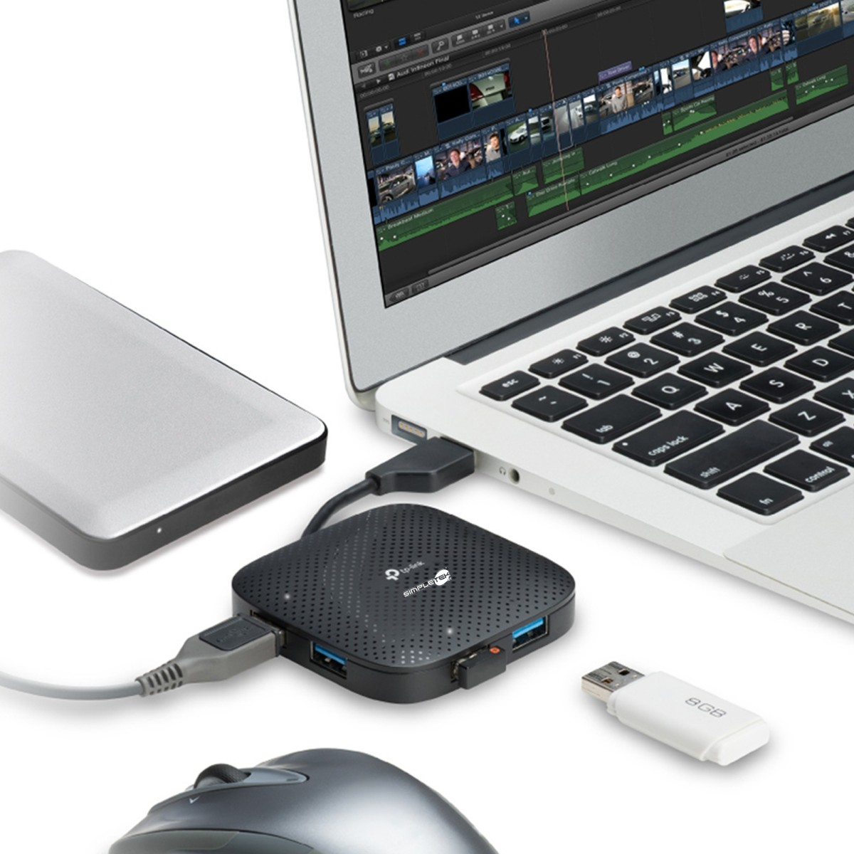 Laptop mit Videoschnittsoftware, USB-Hub, Festplatte, Maus und USB-Stick auf weißer Oberfläche.