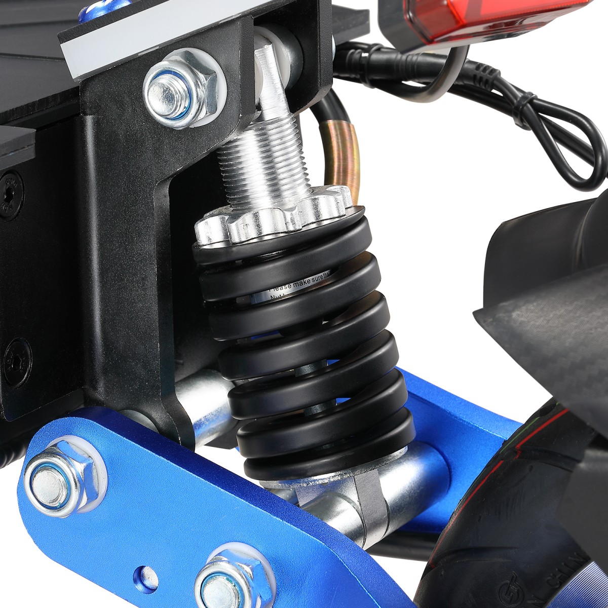 Zbliżenie systemu zawieszenia skutera. Czarna sprężyna jest ściśnięta pomiędzy niebieskimi i czarnymi elementami metalowymi, ze śrubami i nakrętkami.