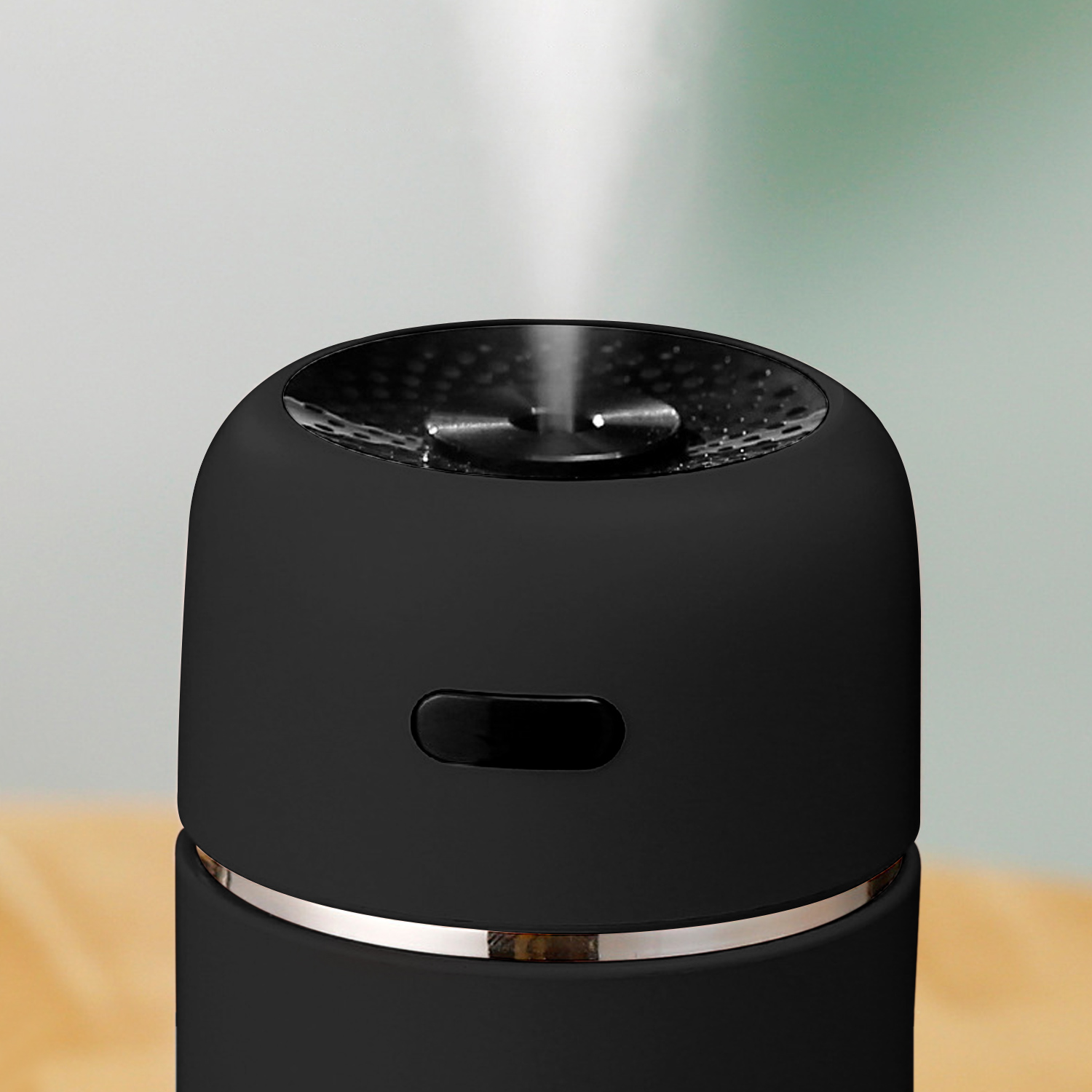 Czarny nawilżacz emituje parę. Ma srebrny pierścień u podstawy i czarny przycisk. Tło jest rozmyte zielone.