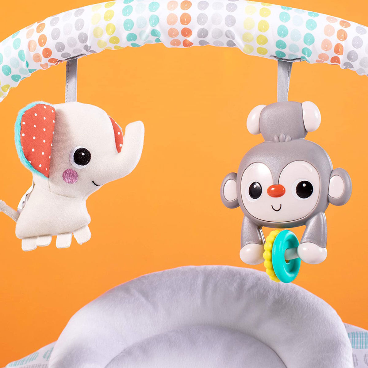 Un mobile per bambini con un elefante e una scimmia giocattolo. Lo sfondo è arancione. I giocattoli sono appesi a un arco a pois.