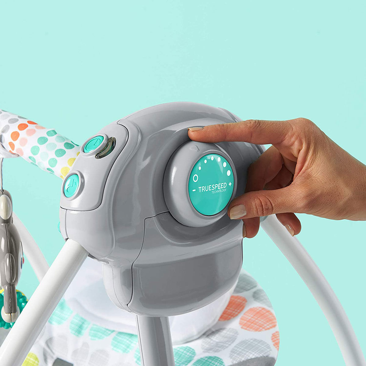 Una mano regola il controllo di un'altalena per bambini. L'altalena è grigia e bianca con bottoni turchesi e un quadrante verde acqua con punti bianchi.