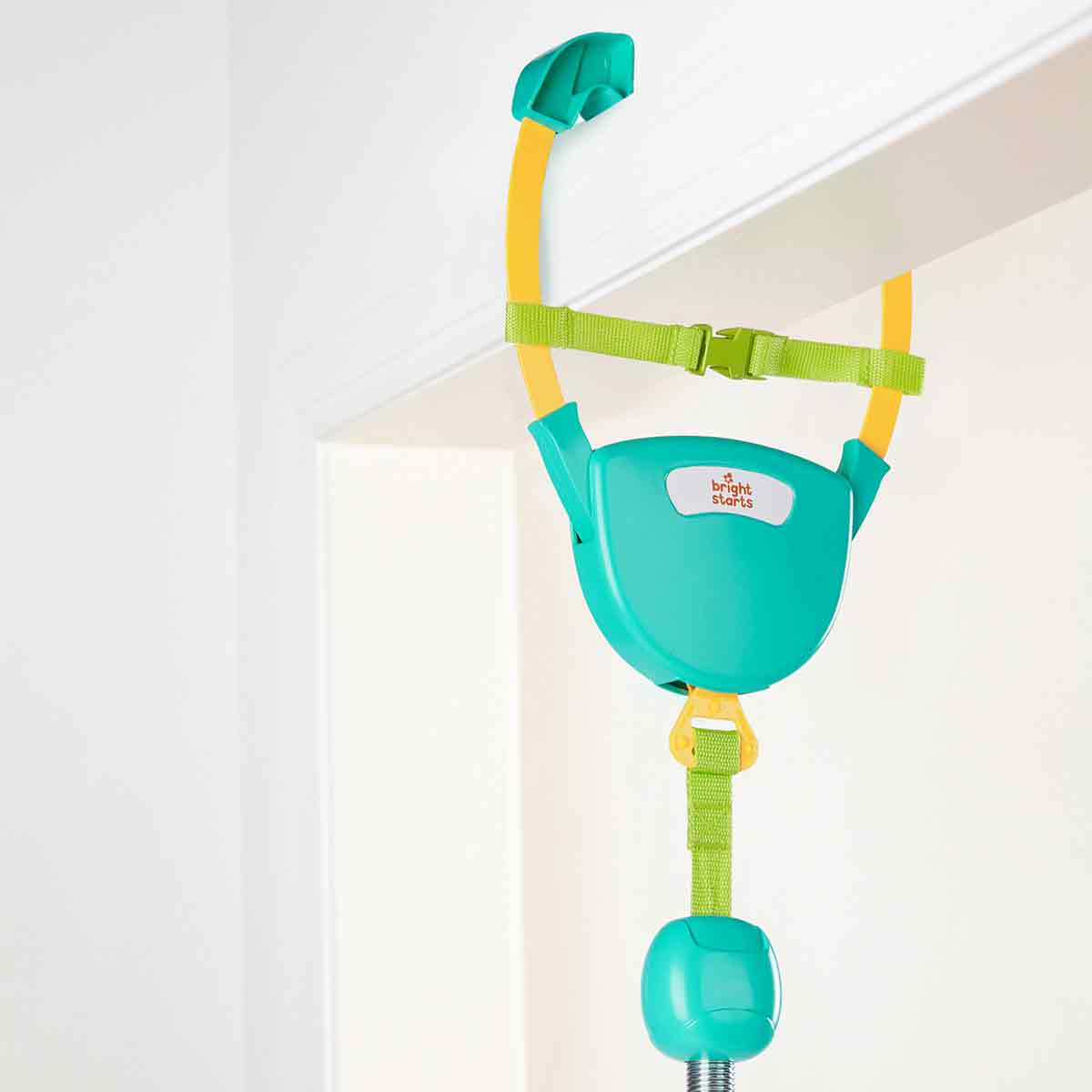 Un saltador para bebés colgando de un marco de puerta. Es turquesa, amarillo y verde. Se ve la marca 'bright starts'.