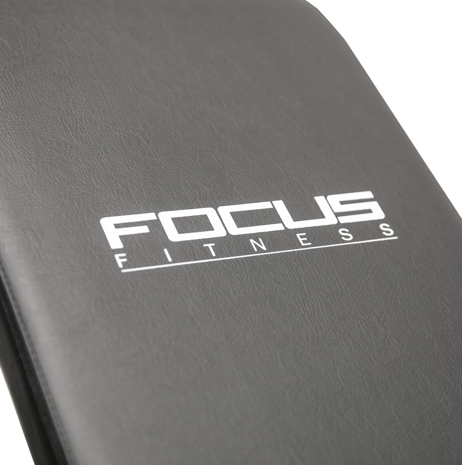 Close-up van een grijze fitnessbank met de woorden "FOCUS FITNESS" in het wit. De bank staat schuin en toont het getextureerde oppervlak.