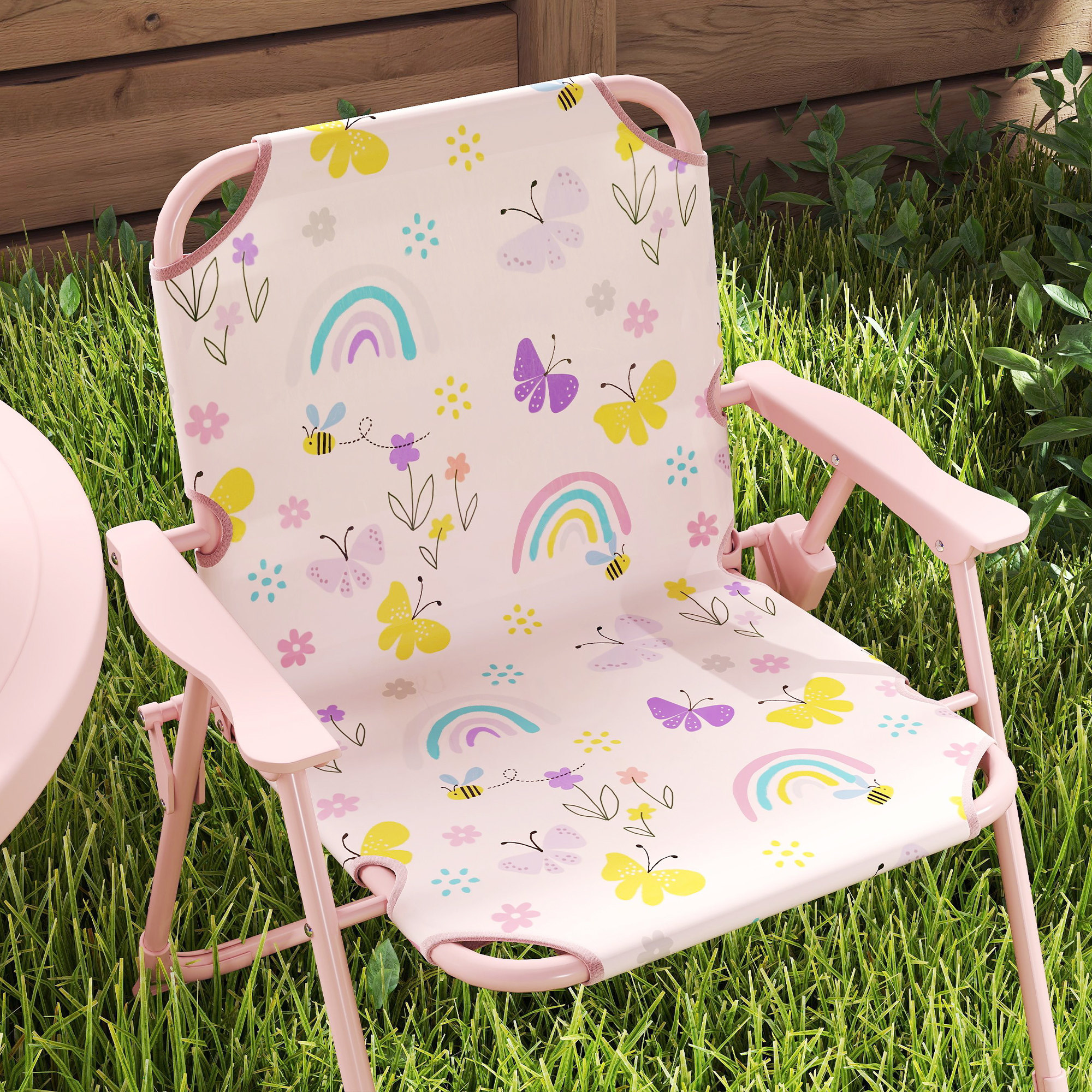 Sedia rosa per bambini con farfalle e arcobaleni sull'erba. Staccionata in legno sullo sfondo.