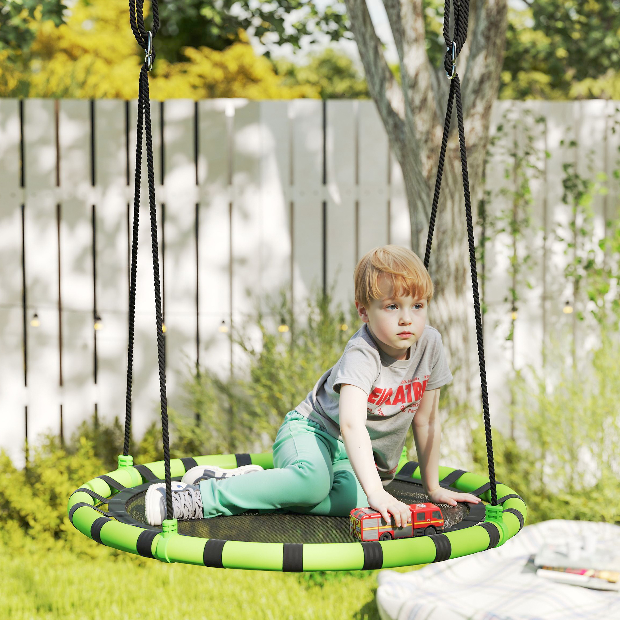 Un niño en un columpio sostiene un coche de juguete. El columpio está en un jardín con una valla blanca y hierba verde.
