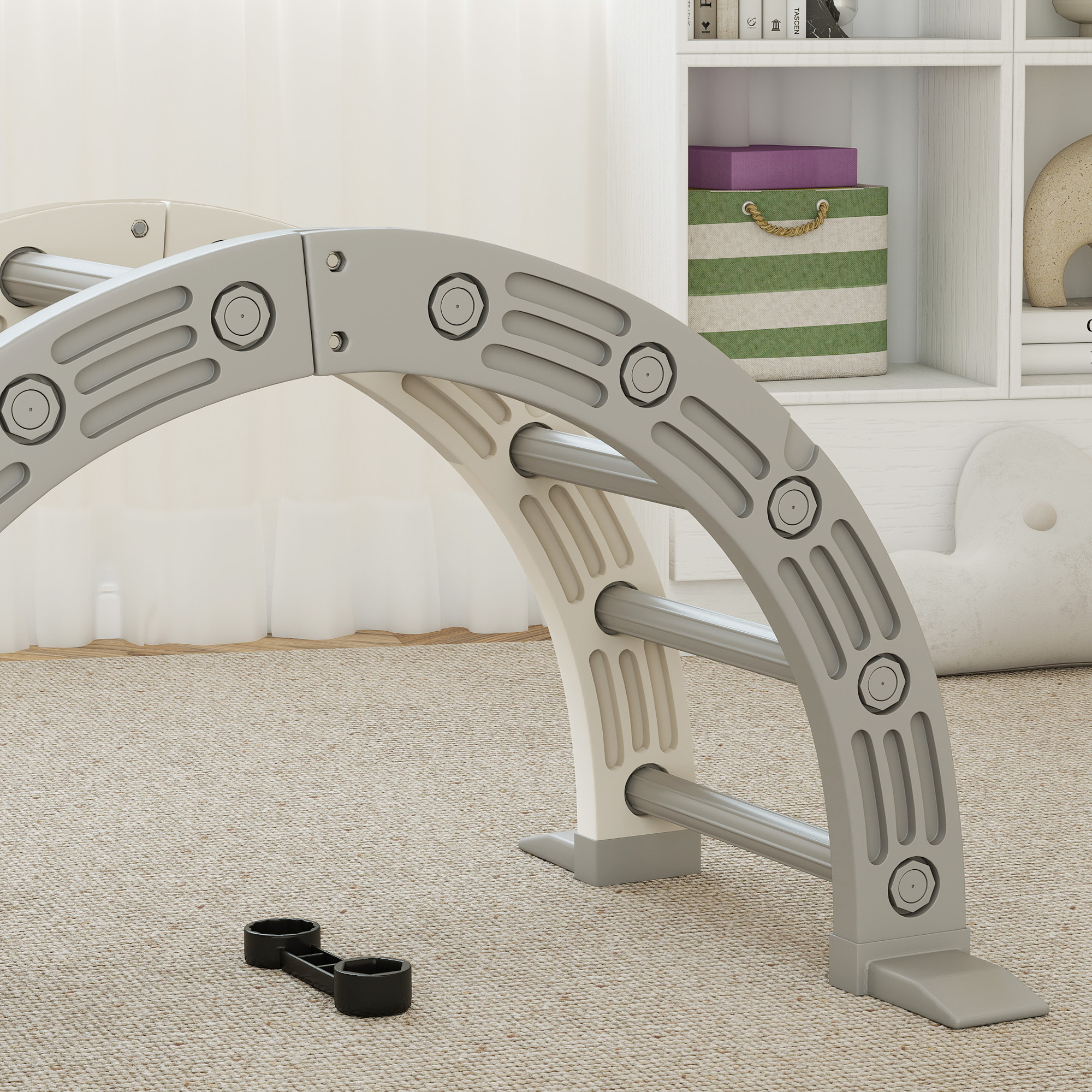 Un arco de escalada gris y blanco sobre una alfombra beige. Una herramienta negra delante. Un estante con juguetes al fondo.