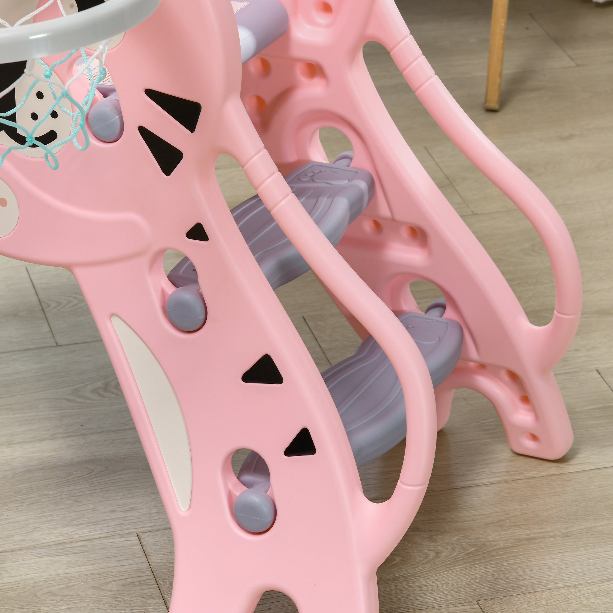 Un tobogán infantil de plástico rosa con aro de baloncesto. El tobogán tiene escalones grises y detalles triangulares negros.