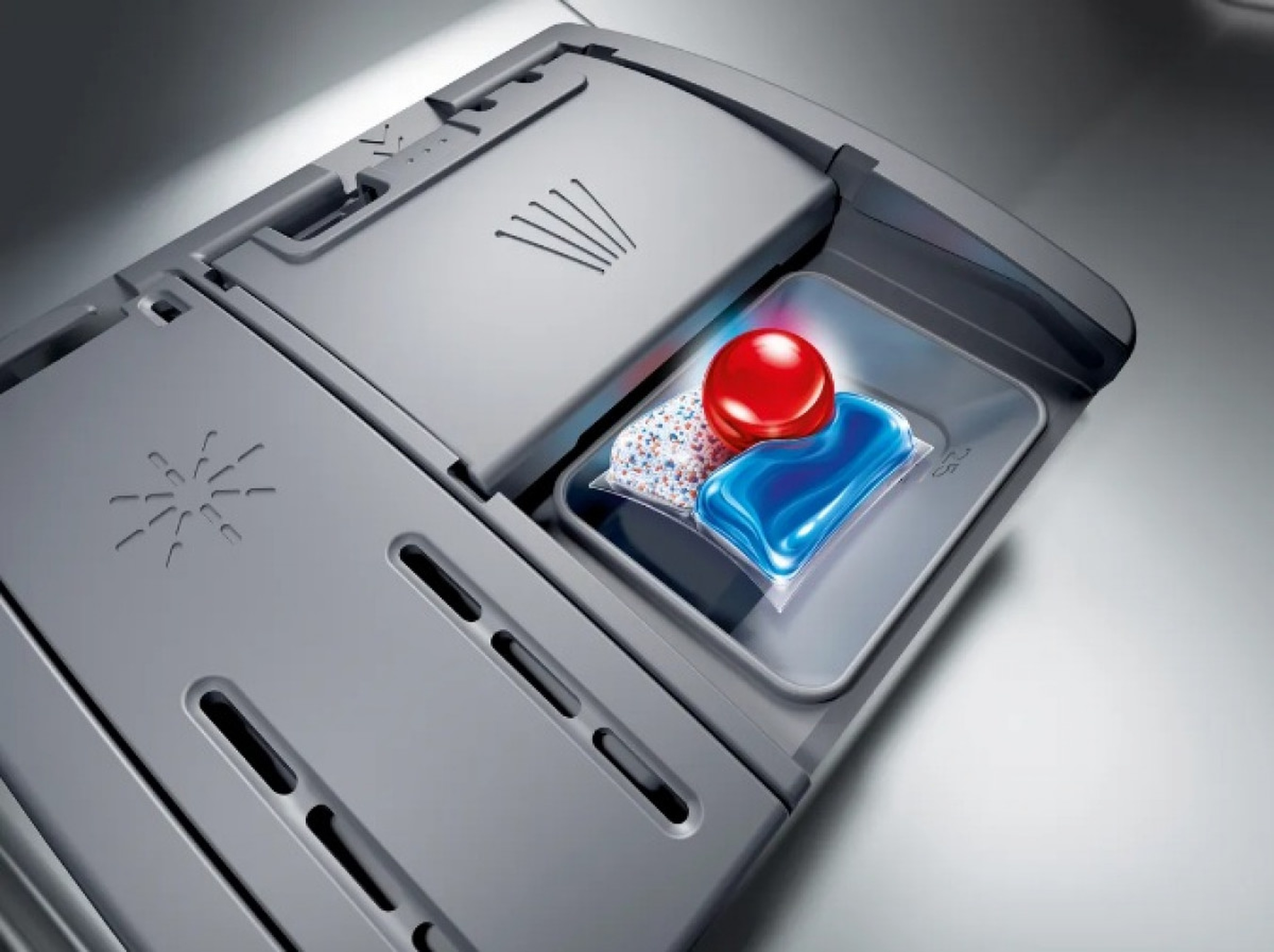 Komora zmywarki z kapsułkami do mycia naczyń. Zawiera czerwoną kulkę i niebiesko-białe opakowania detergentów.