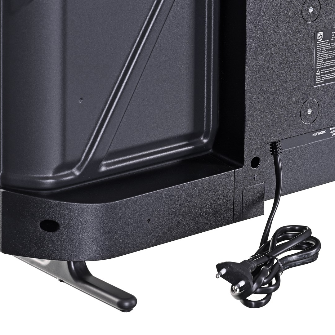 Zbliżenie na tył czarnego telewizora, stojak i przewód zasilający. Przewód jest zwinięty, a wtyczka jest widoczna.