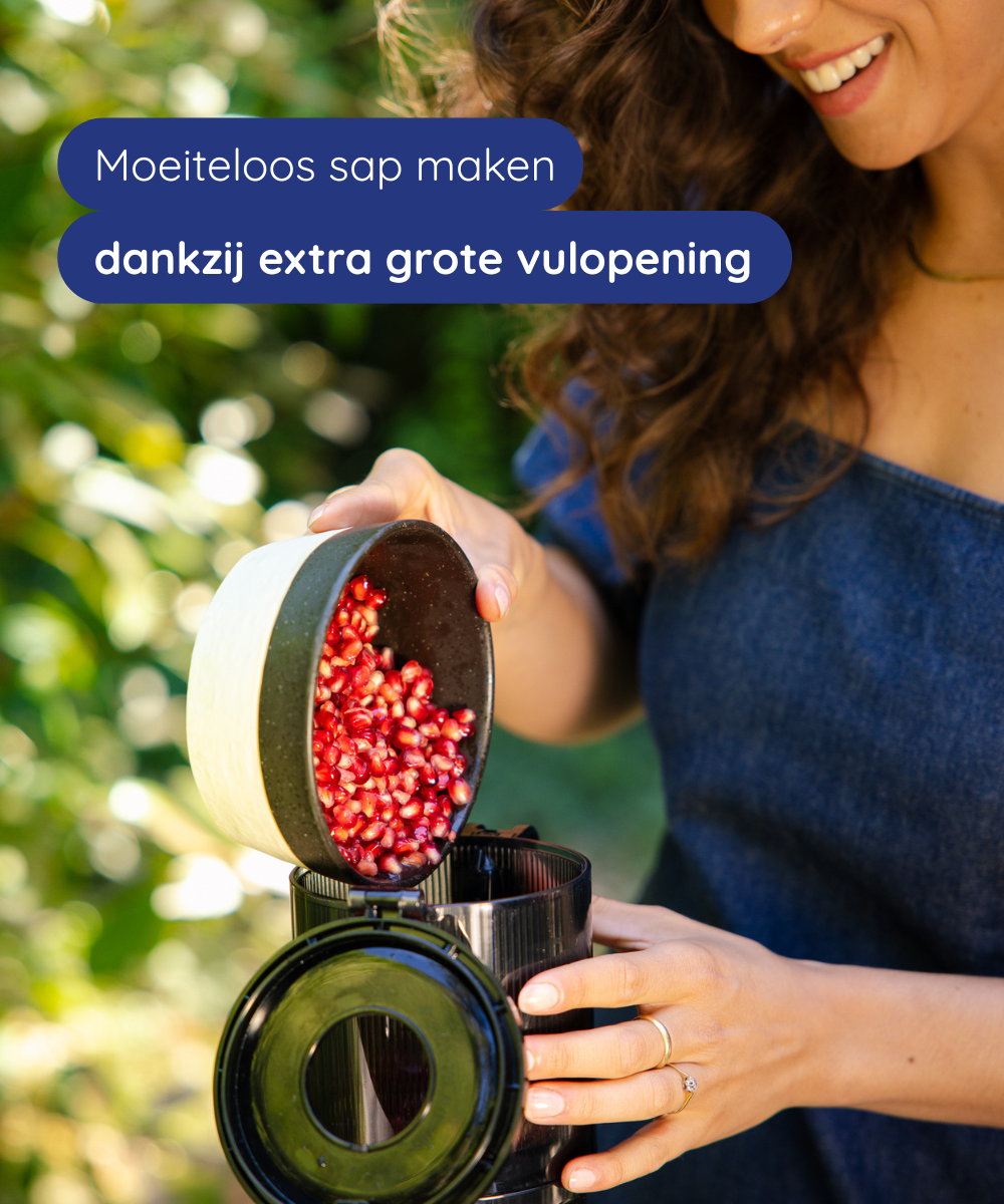 A woman pours pomegranate seeds into a juicer. The juicer is black, the seeds are red. The woman is smiling.