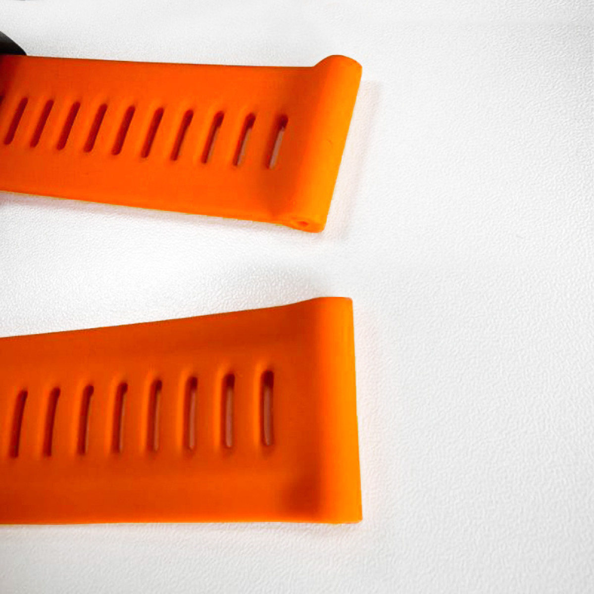 Zwei orangefarbene Uhrenarmbänder mit Lüftungsschlitzen auf einer weißen, strukturierten Oberfläche. Das obere Band überlappt das untere.