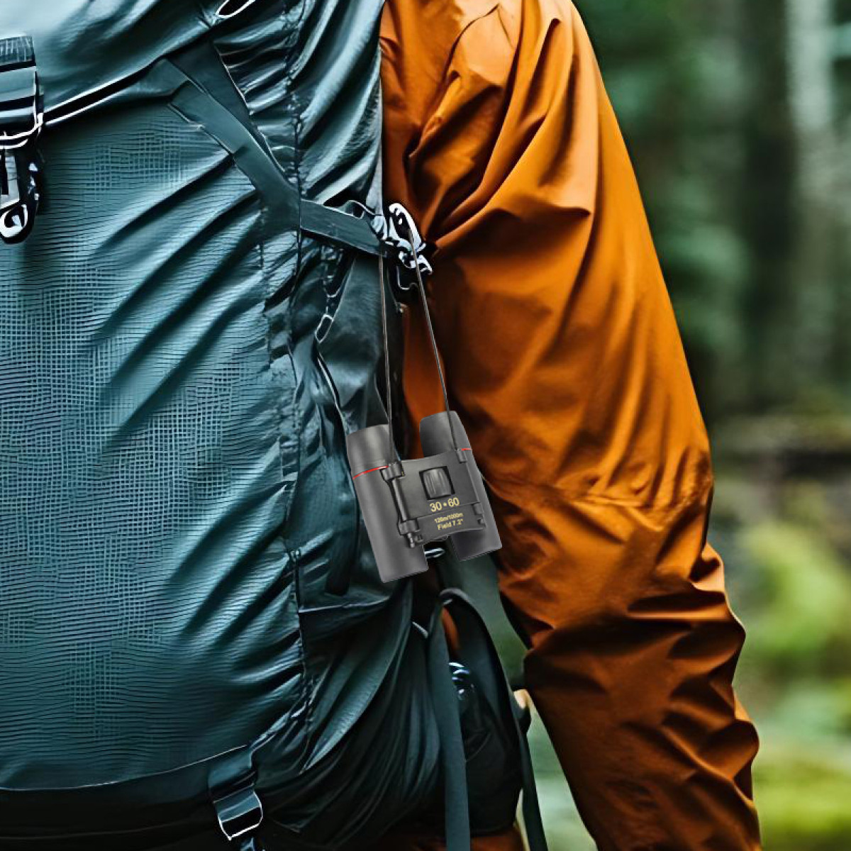 Osoba z plecakiem i pomarańczową kurtką. Czarne lornetki z czerwonymi akcentami wiszą na plecaku.