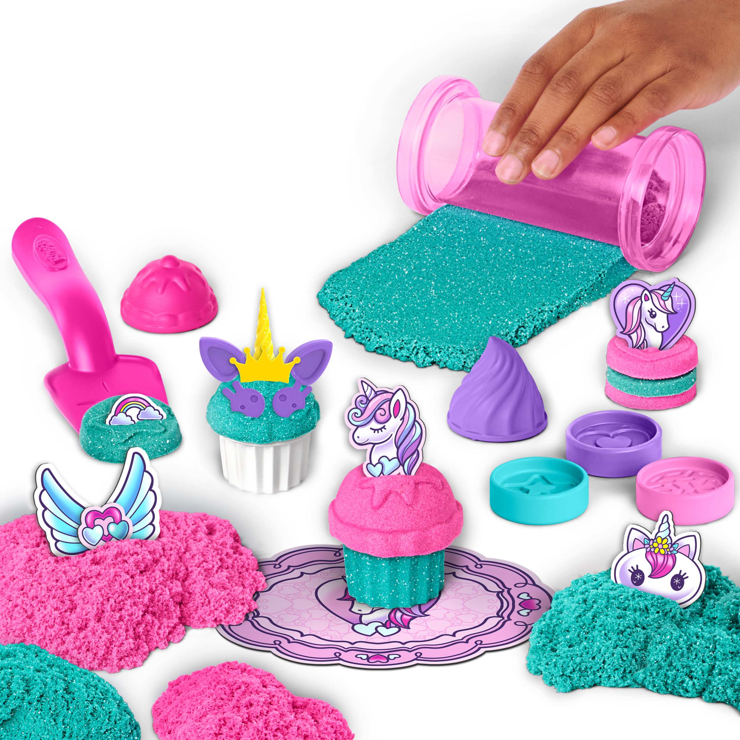 Una mano vierte arena rosa de un recipiente. Juego temático de unicornios con arena rosa y verde azulado, moldes y accesorios.