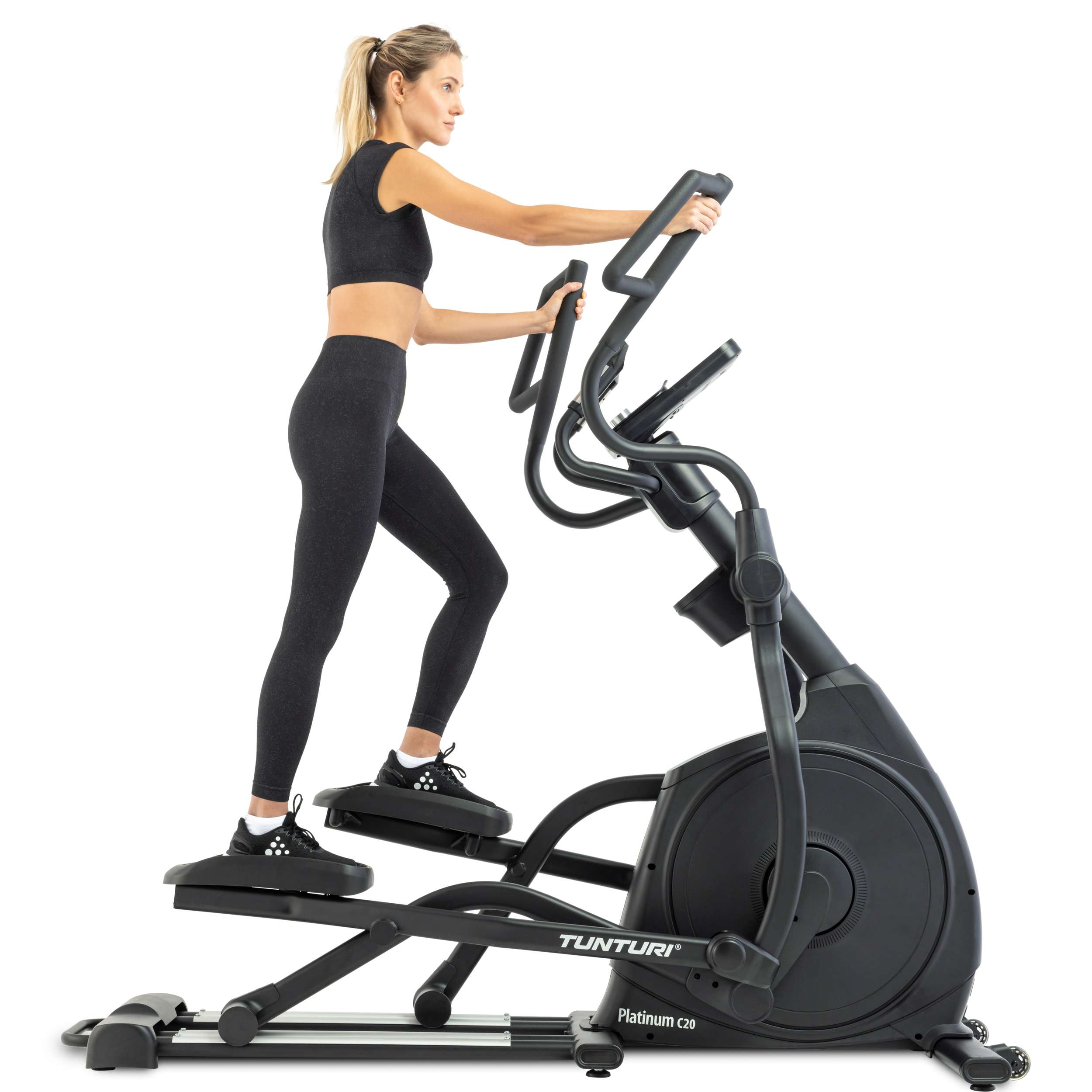 A woman exercises on a black elliptical machine. She wears black athletic attire. White background.