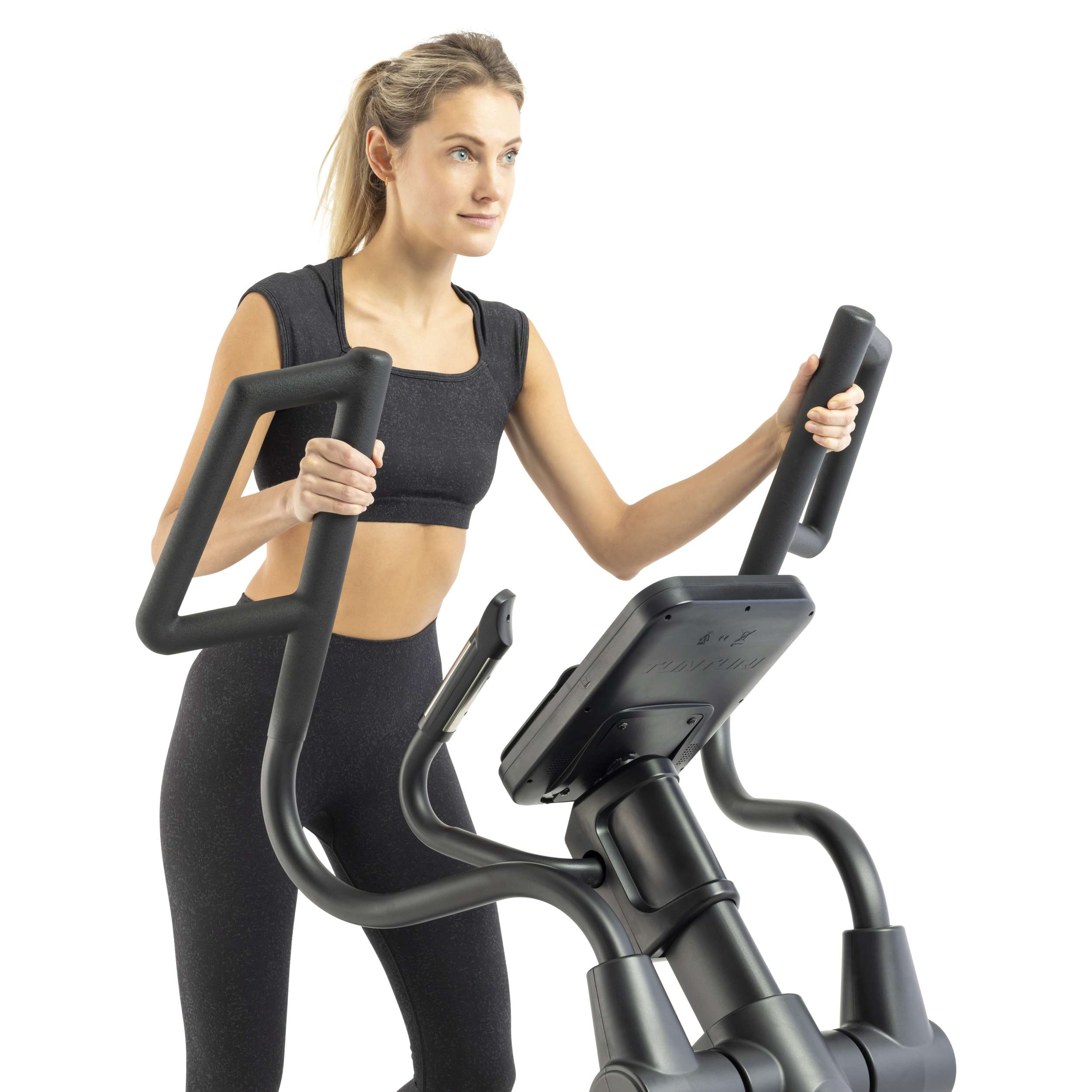 A woman exercises on a black elliptical machine. She wears black workout clothes. The background is white.