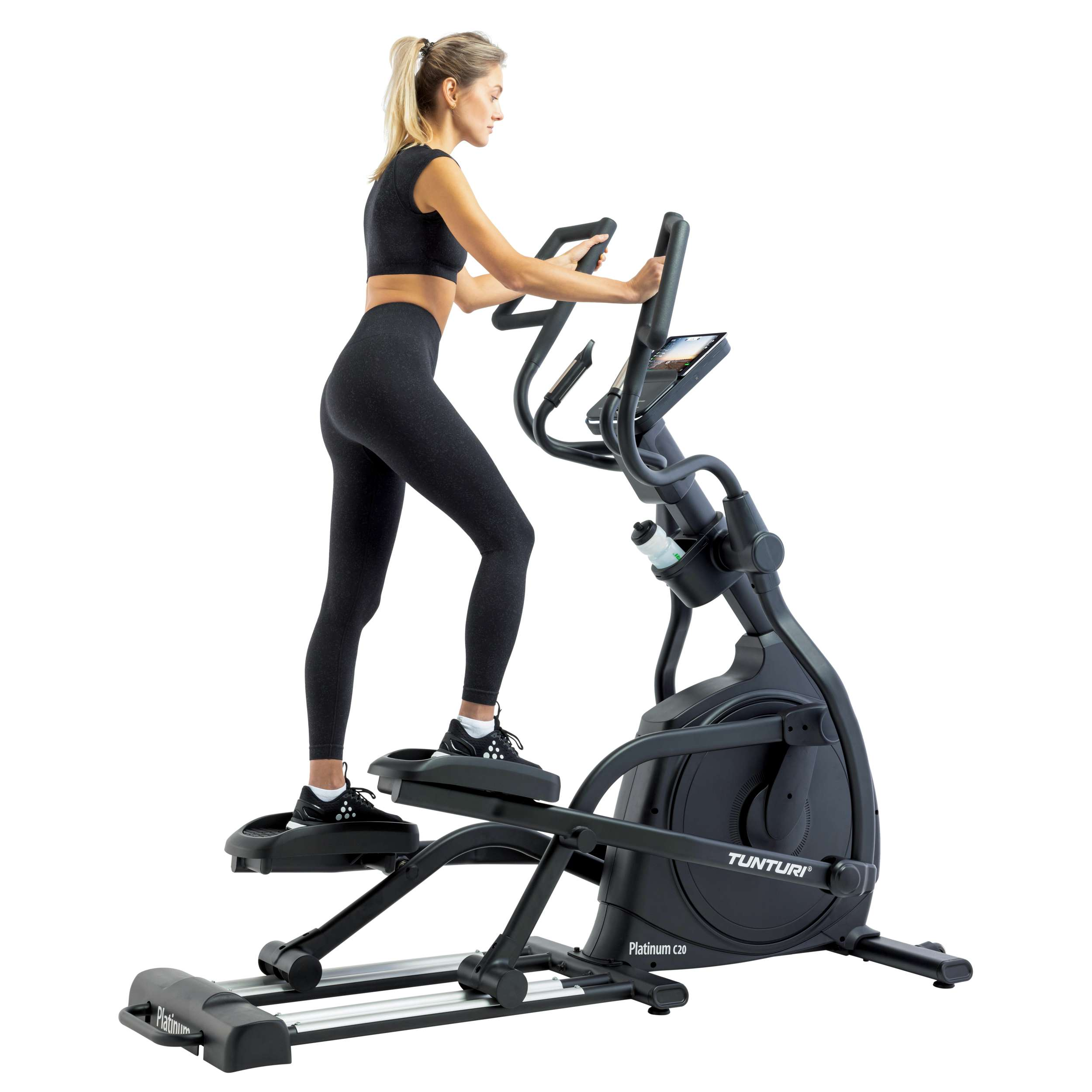 Woman in black workout clothes using a black elliptical machine. White background. A bottle of water is on the machine.