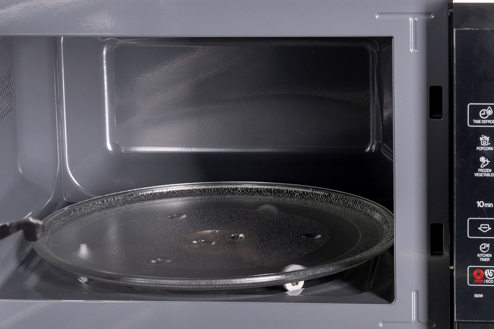 Interno di un microonde. Un piatto di vetro è sul fondo. Il pannello di controllo è sul lato destro. Interno grigio.