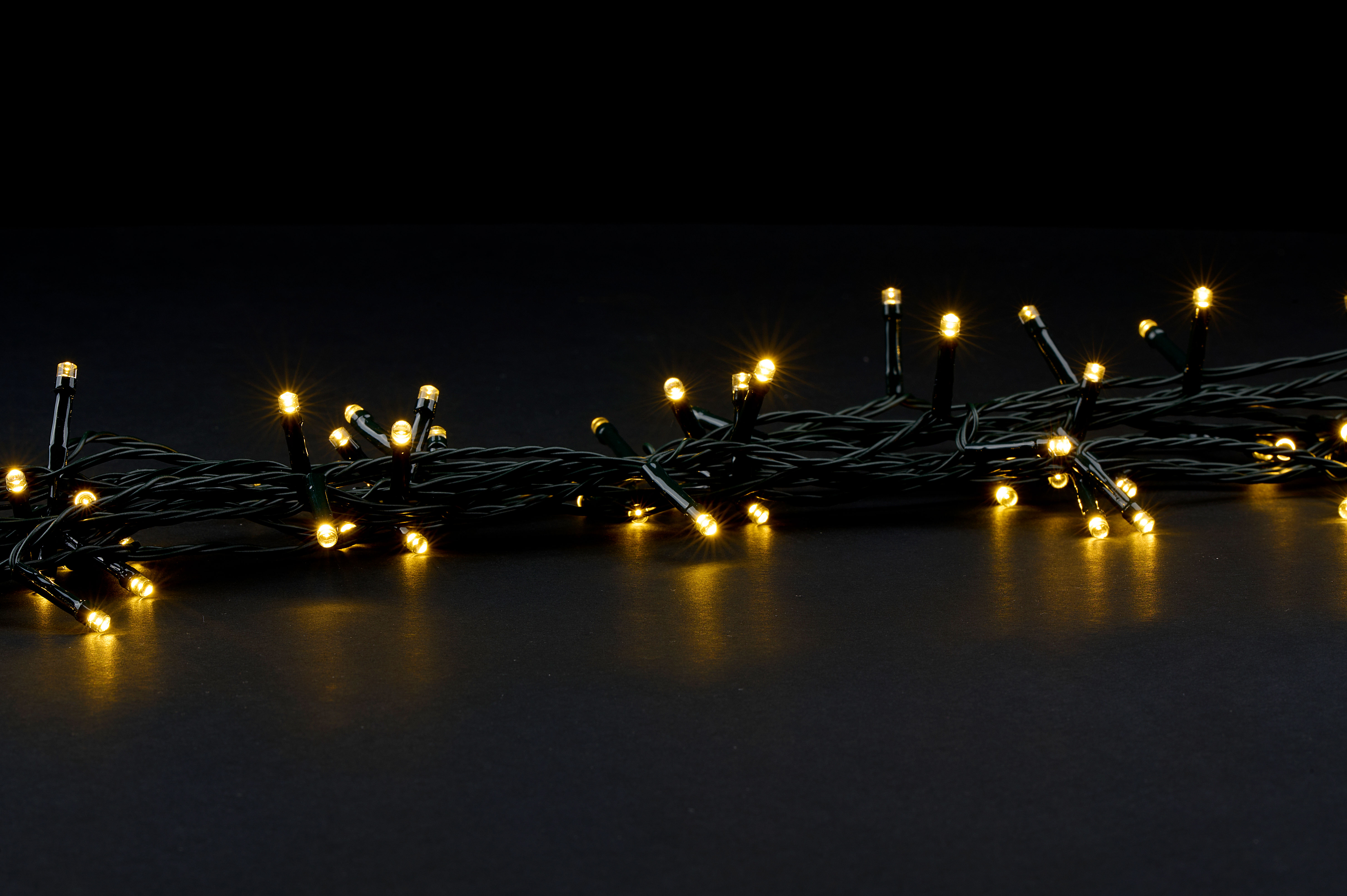 Guirlande de lumières jaunes sur fond noir. Les lumières sont petites et brillantes. Les fils sont vert foncé.