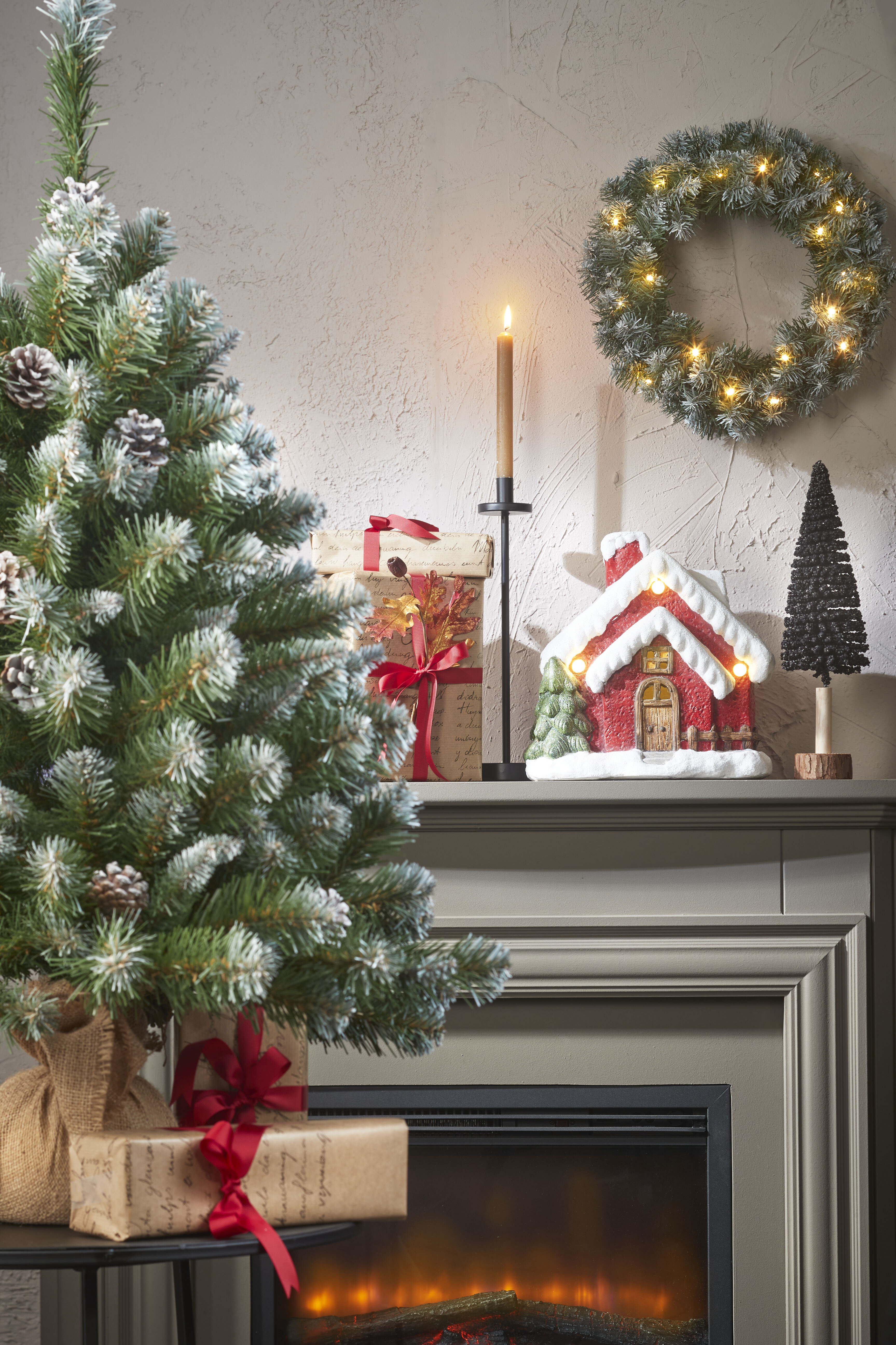 Une scène de Noël décorée avec un arbre, des cadeaux, une cheminée, une bougie et une couronne.