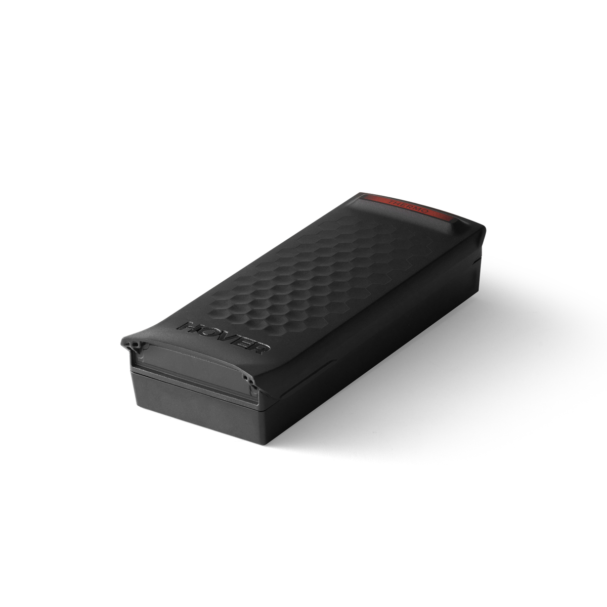 Czarne prostokątne urządzenie z teksturowanym wierzchem, napisem 'HOVER' i czerwonym światłem. Leży na białej powierzchni.