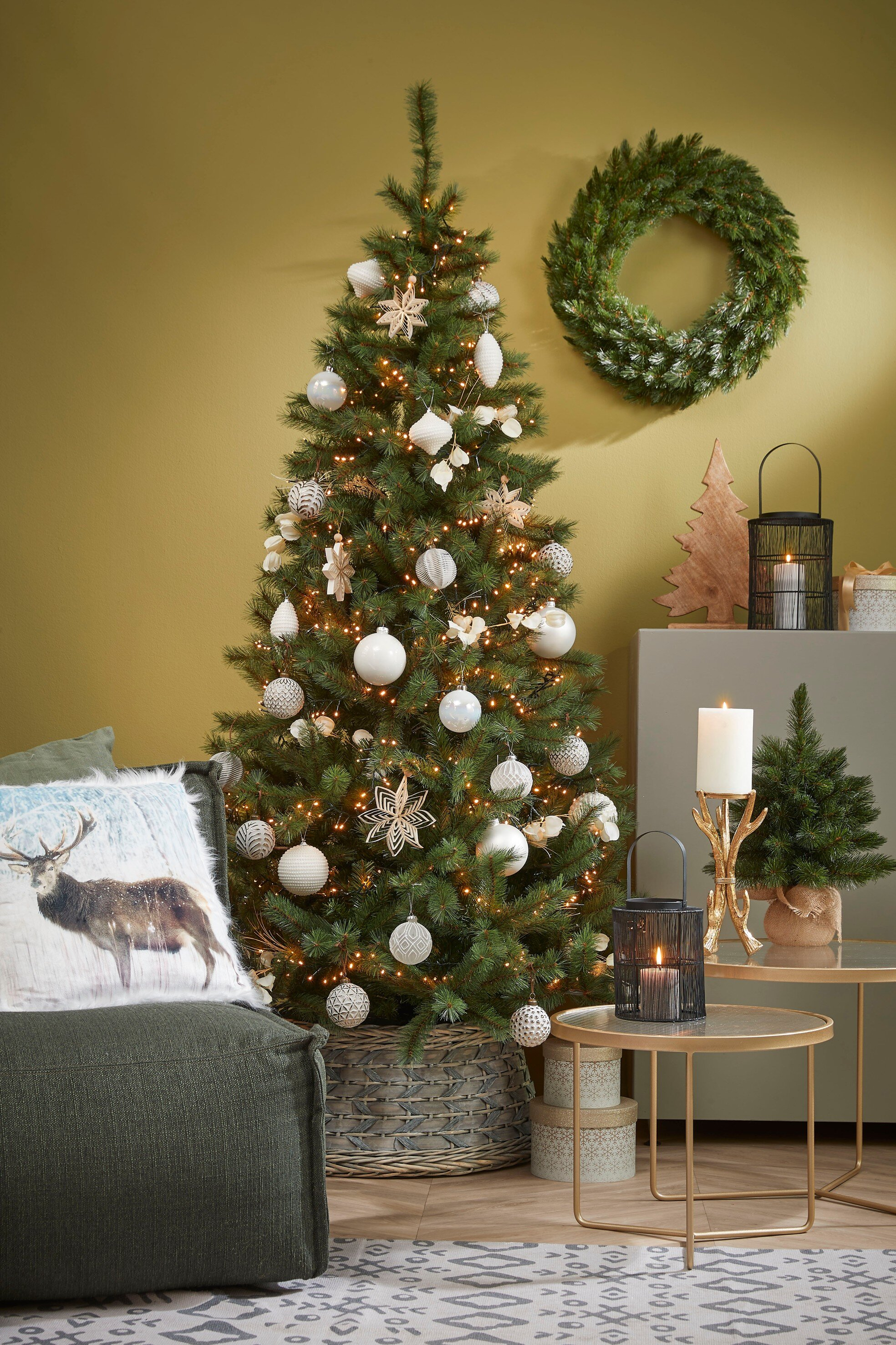 Un sapin de Noël décoré est central, avec des ornements, des lumières et une couronne. Un canapé avec un coussin de cerf est à gauche.