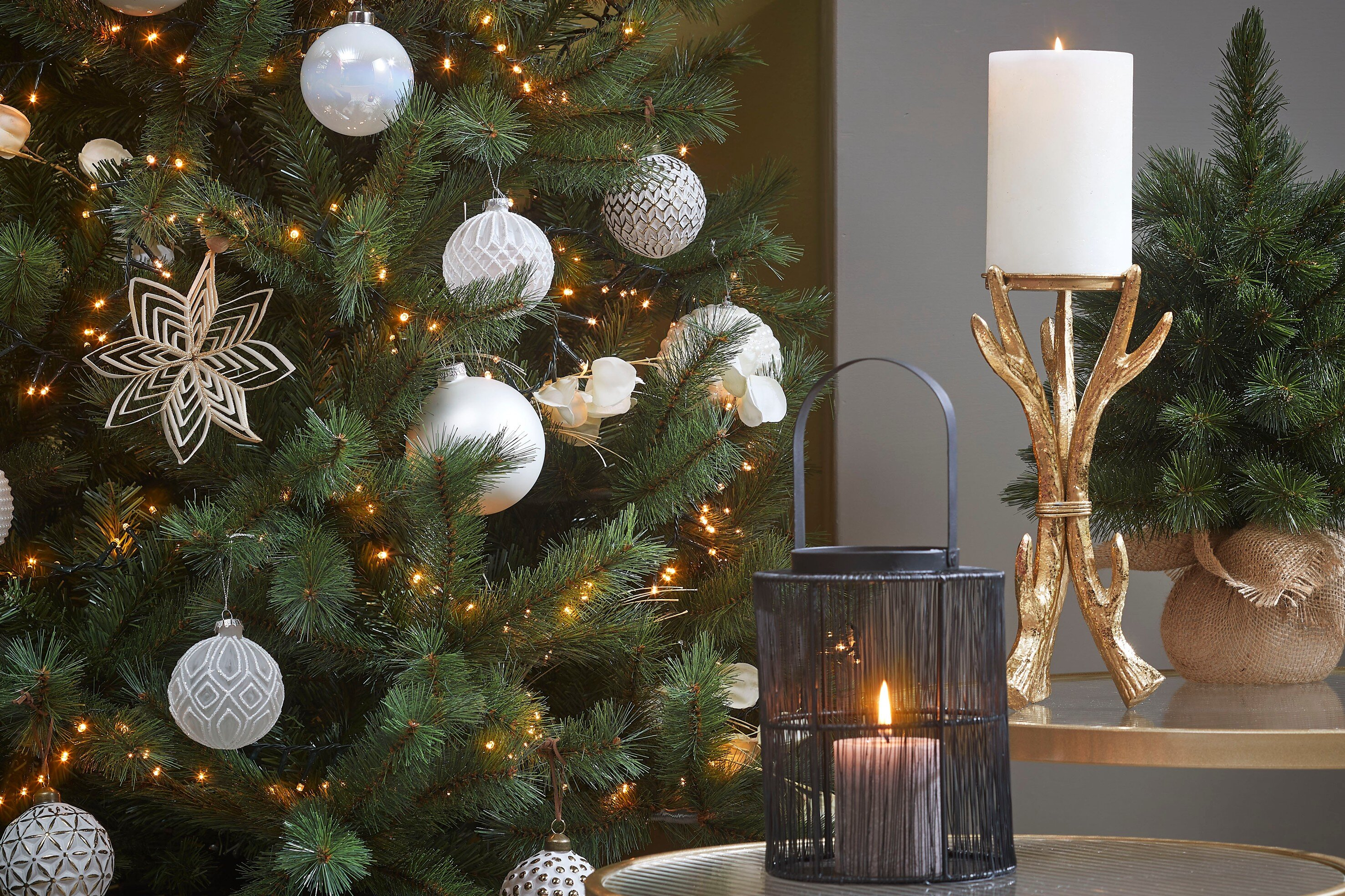 Un arbre de Noël décoré avec des ornements, une bougie et une lanterne sur une table. Ambiance festive.