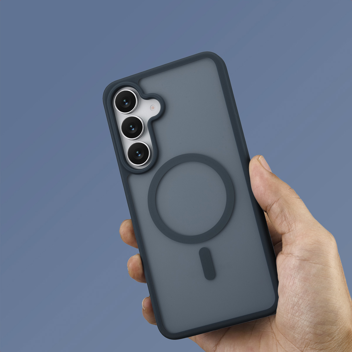 Een hand die een telefoon in een grijze hoes vasthoudt. De hoes heeft een cirkelvormig ontwerp en drie cameralenzen. De achtergrond is blauw.