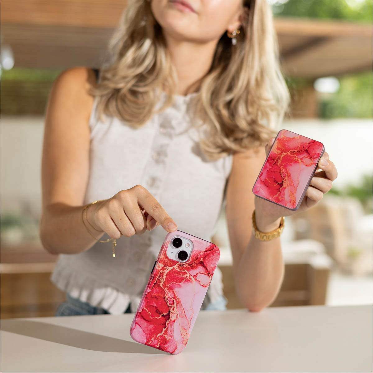 Vrouw met twee telefoonhoesjes. De hoesjes hebben een rood en roze marmerontwerp. Eén wordt met een vinger aangewezen.