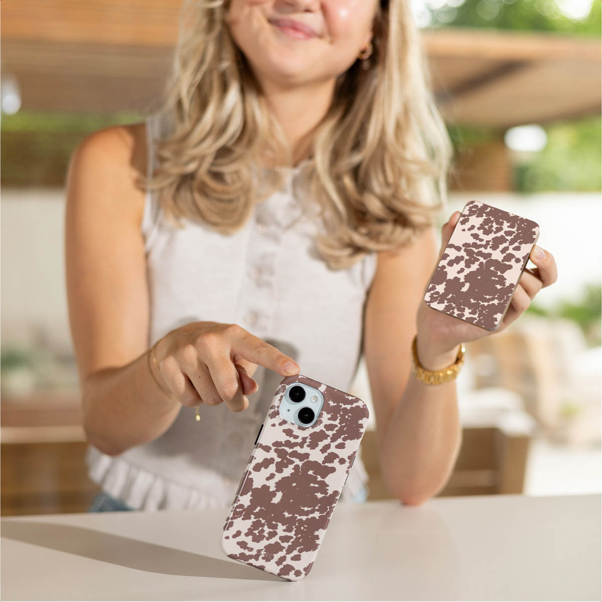 Een vrouw houdt twee telefoonhoesjes met koeienprint vast. Eén hoesje in haar hand, de andere op tafel.