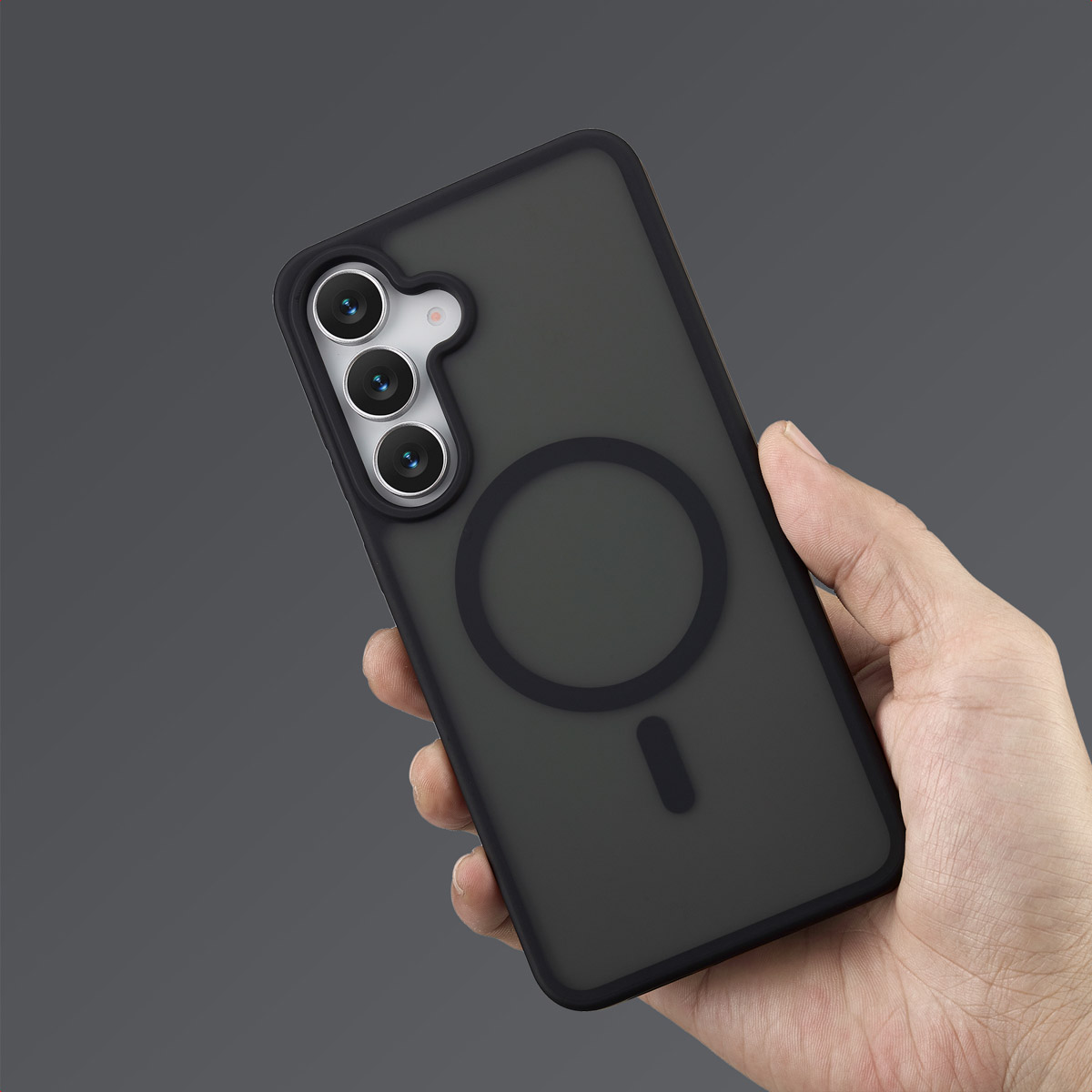 Een hand houdt een zwarte telefoonhoes vast met een telefoon erin. De hoes heeft een uitsparing voor de camera en een magnetische ring.