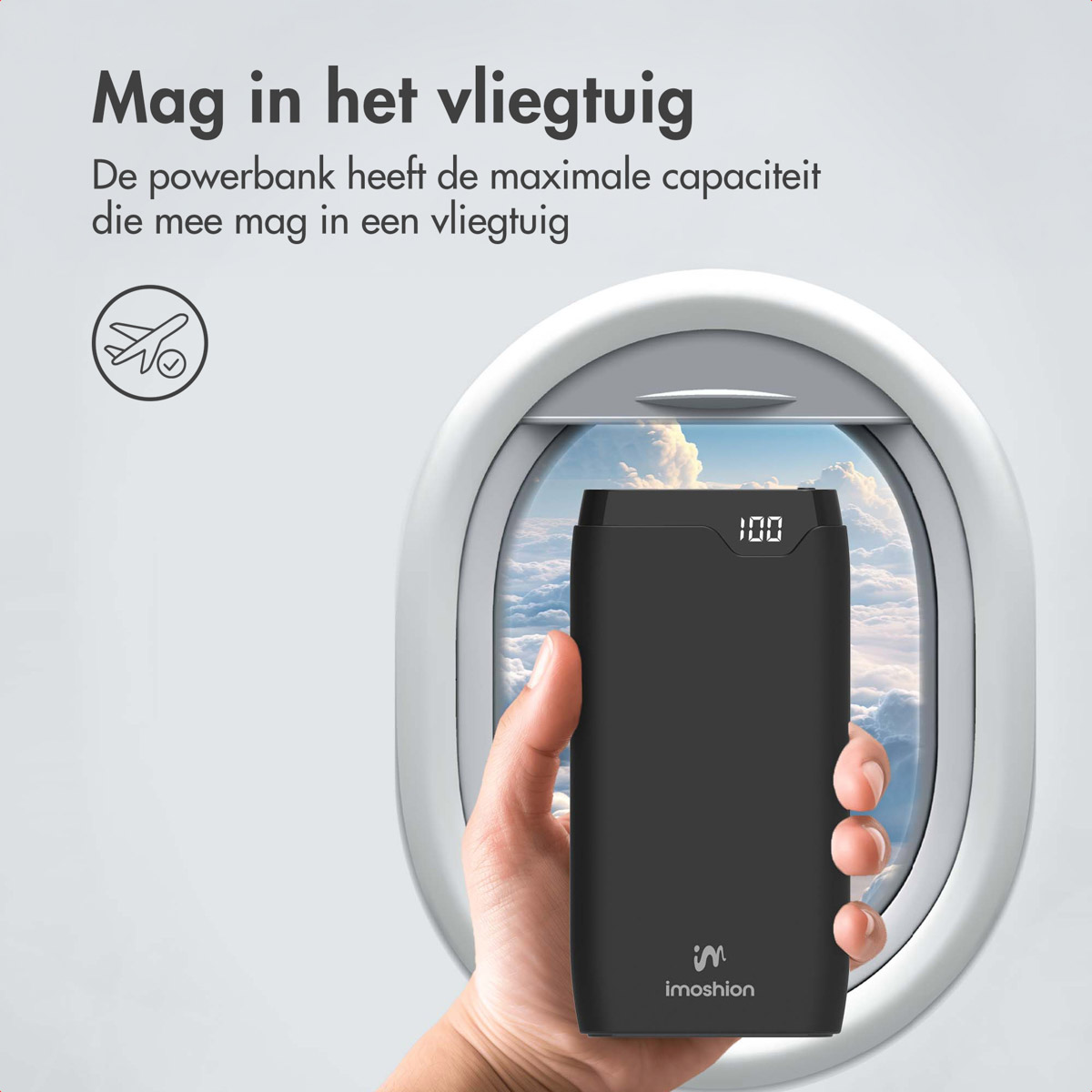 Une main tient une batterie externe noire devant une fenêtre d'avion, affichant 100 à l'écran. L'arrière-plan montre des nuages.