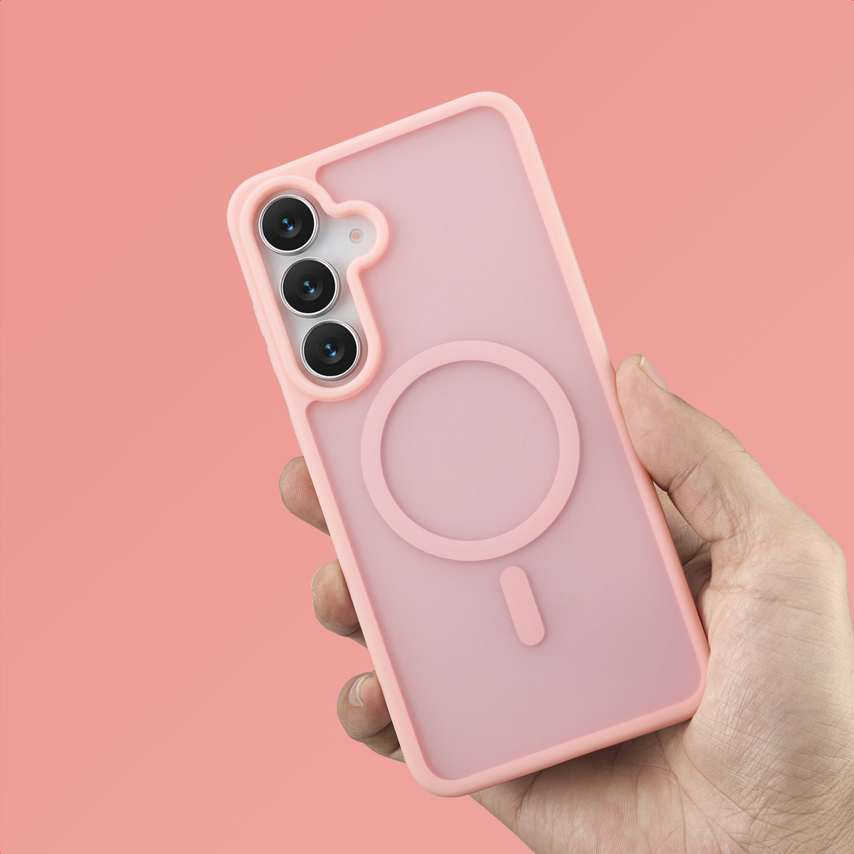 Een hand die een roze telefoonhoes vasthoudt tegen een roze achtergrond. De hoes heeft een cirkelvormig ontwerp en camera-uitsparingen.