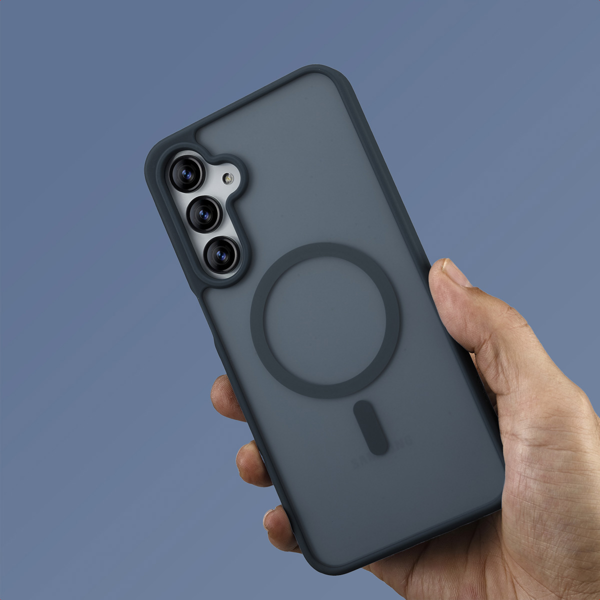 Una mano tiene una custodia per telefono grigio scuro con un attacco magnetico circolare. La custodia ha tre obiettivi. Lo sfondo è blu.