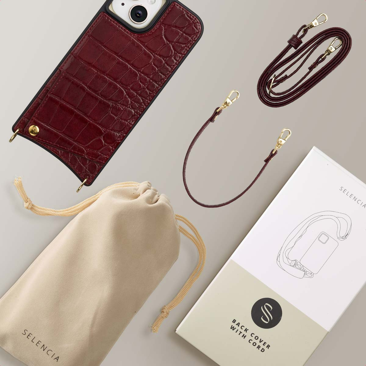 A phone case with a strap, a pouch, and a box, all in burgundy and beige tones. The case has a crocodile leather texture.