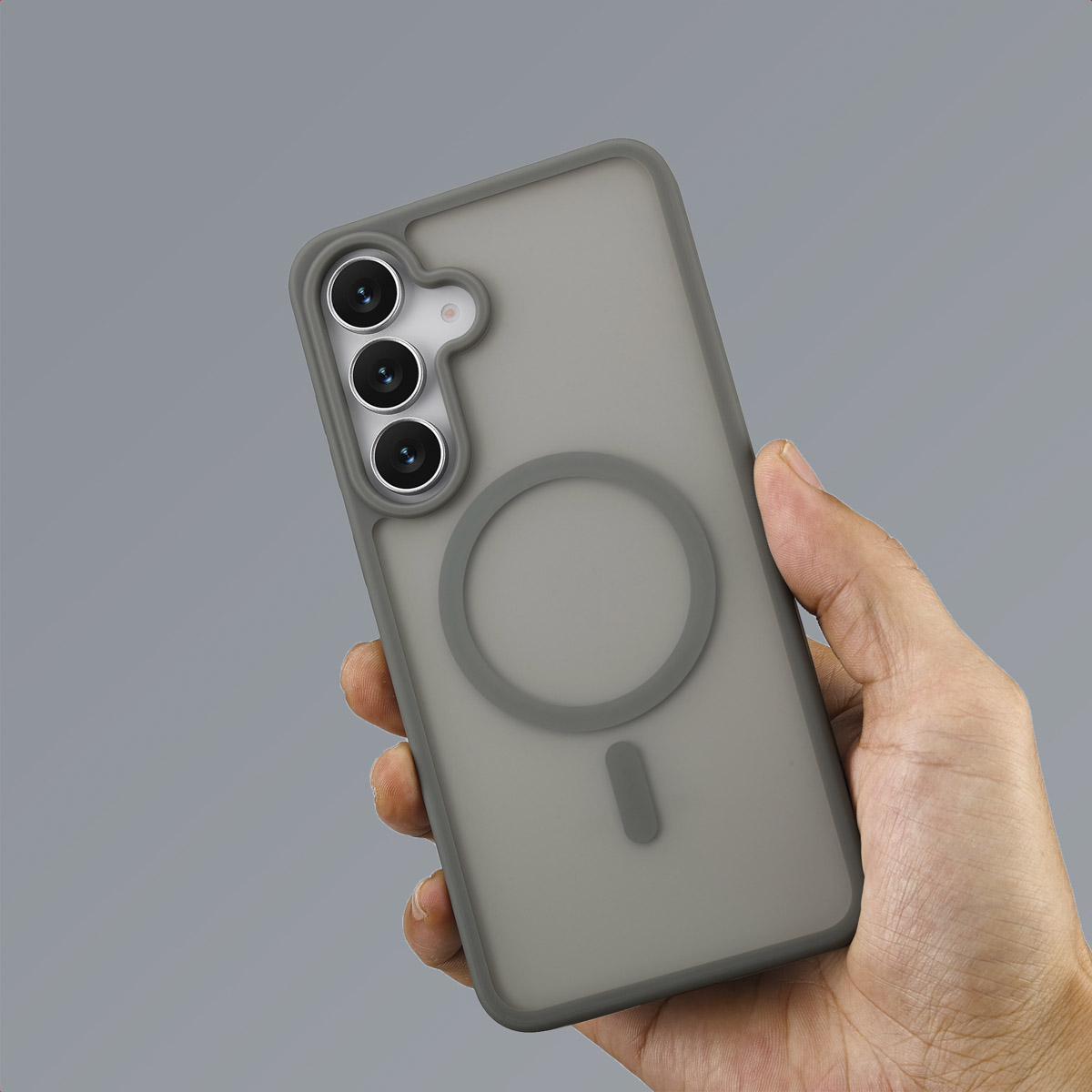 Une main tenant une coque de téléphone grise avec une découpe pour l'appareil photo. La coque a une fixation magnétique circulaire et un rectangle.
