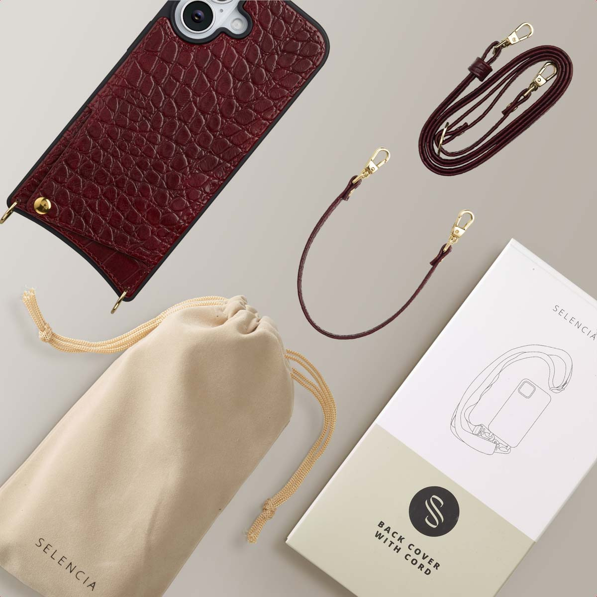 Een telefoonhoesje, een tas en een koord. Het telefoonhoesje is bordeauxrood met gouden accenten. Er is een witte doos met een telefoonillustratie.