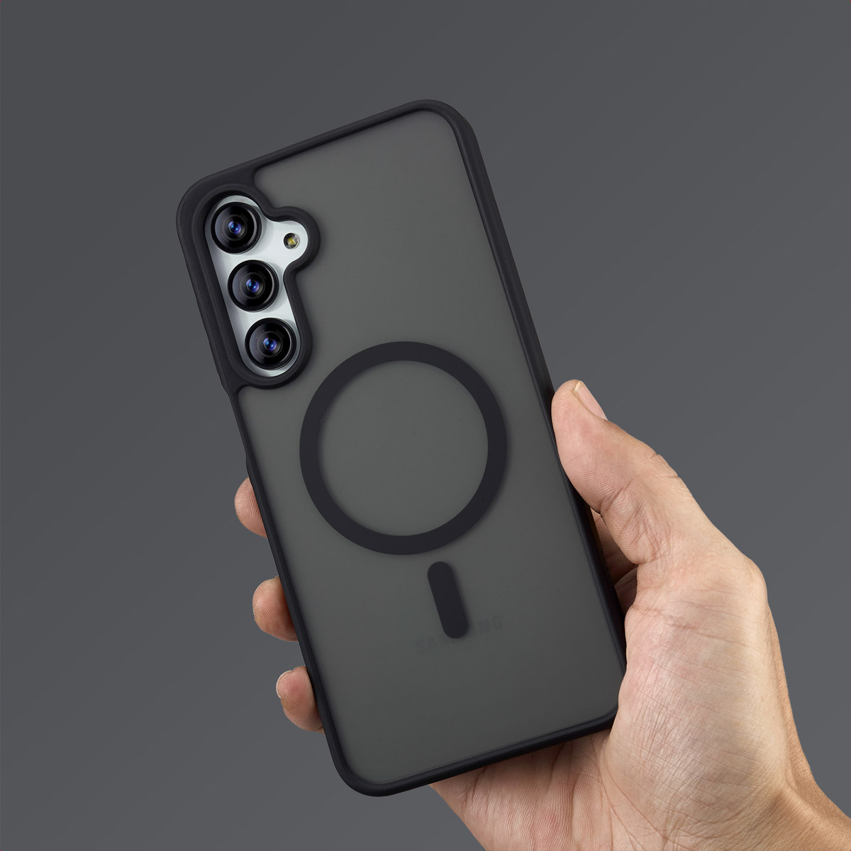 Mano che tiene una custodia grigio scuro con un anello nero e un modulo fotocamera nero. La custodia ha una finitura opaca.
