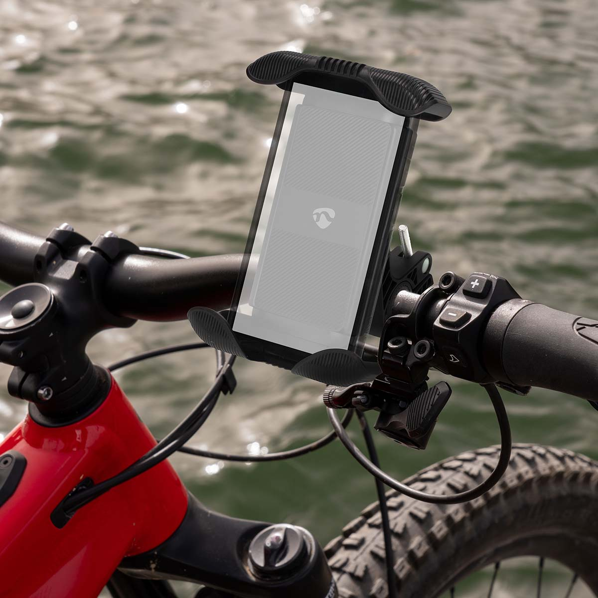 Een fietsstuur met een telefoonhouder. De telefoon toont een logo. De fiets is rood, met een zwart stuur, en de achtergrond is water.