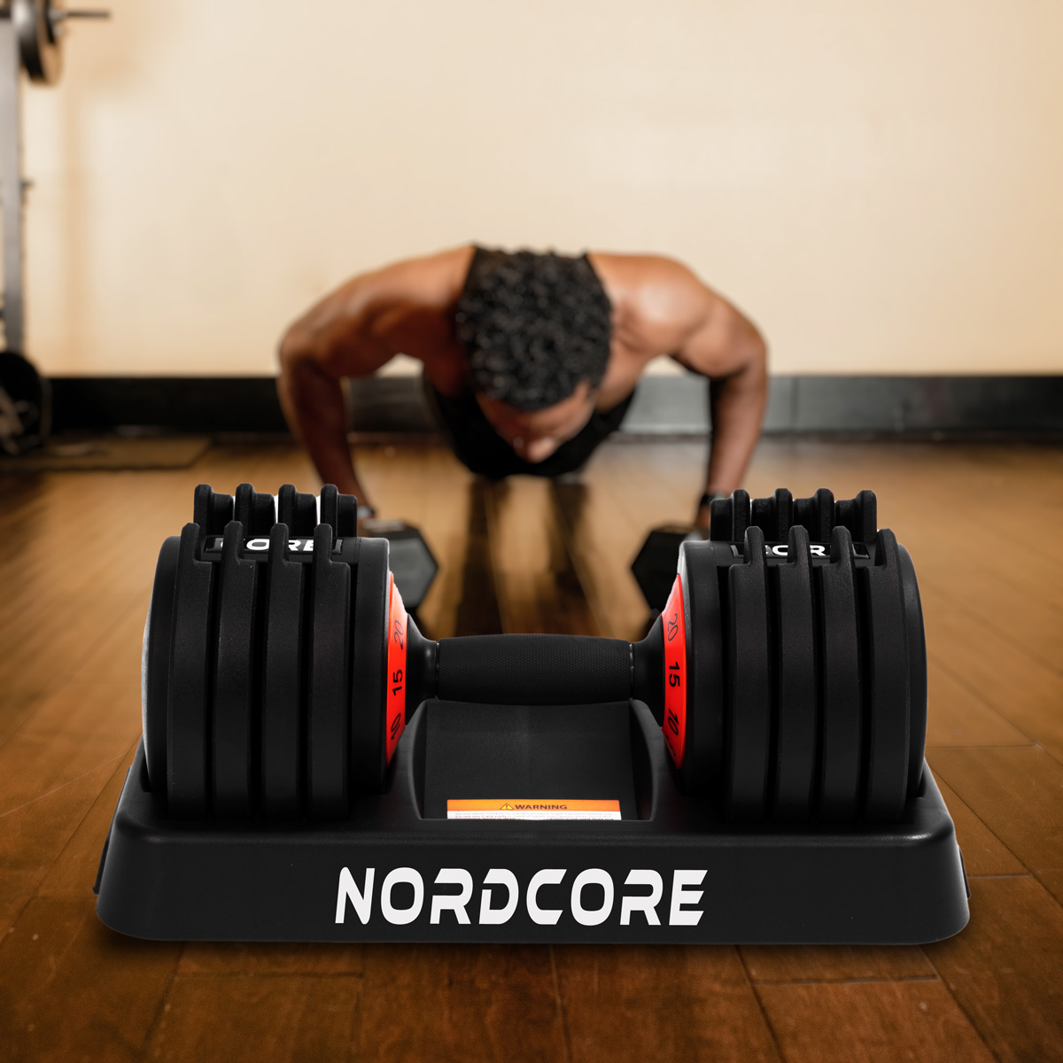 Ein Mann macht Liegestütze in einem Fitnessstudio. Eine Hantel auf einer schwarzen Basis mit dem Wort NORDCORE ist im Vordergrund.