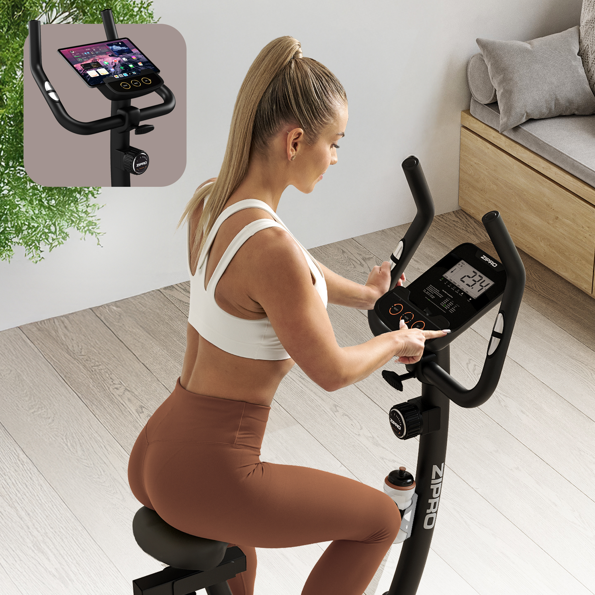 Frau auf dem Heimtrainer, zeigt auf das Display. Das Fahrrad ist schwarz, die Frau trägt ein weißes Oberteil und braune Leggings. Hintergrund: Holzboden.