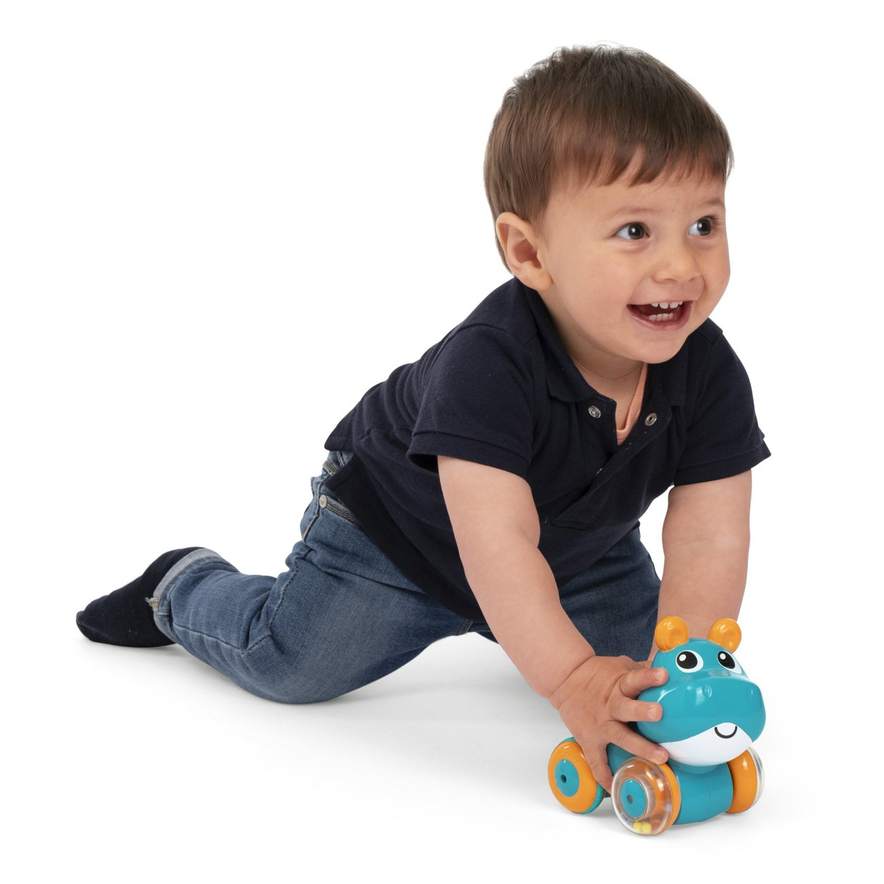 Un niño pequeño sonriente con jeans azules y una camisa azul marino se arrastra hacia un hipopótamo de juguete. El hipopótamo es azul, naranja y blanco.