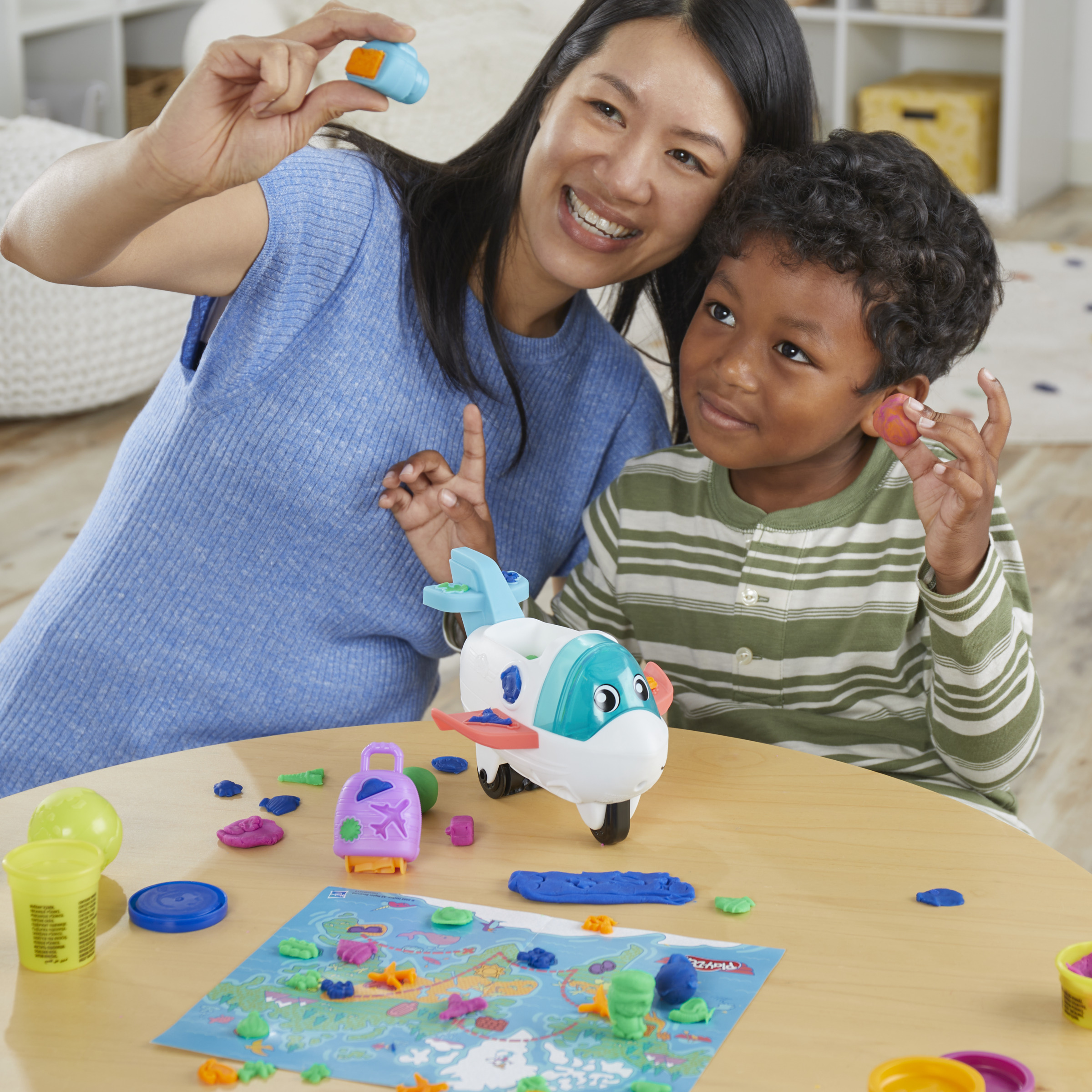 Una mujer y un niño jugando con plastilina. Están sonriendo. Hay un avión de juguete en la mesa.