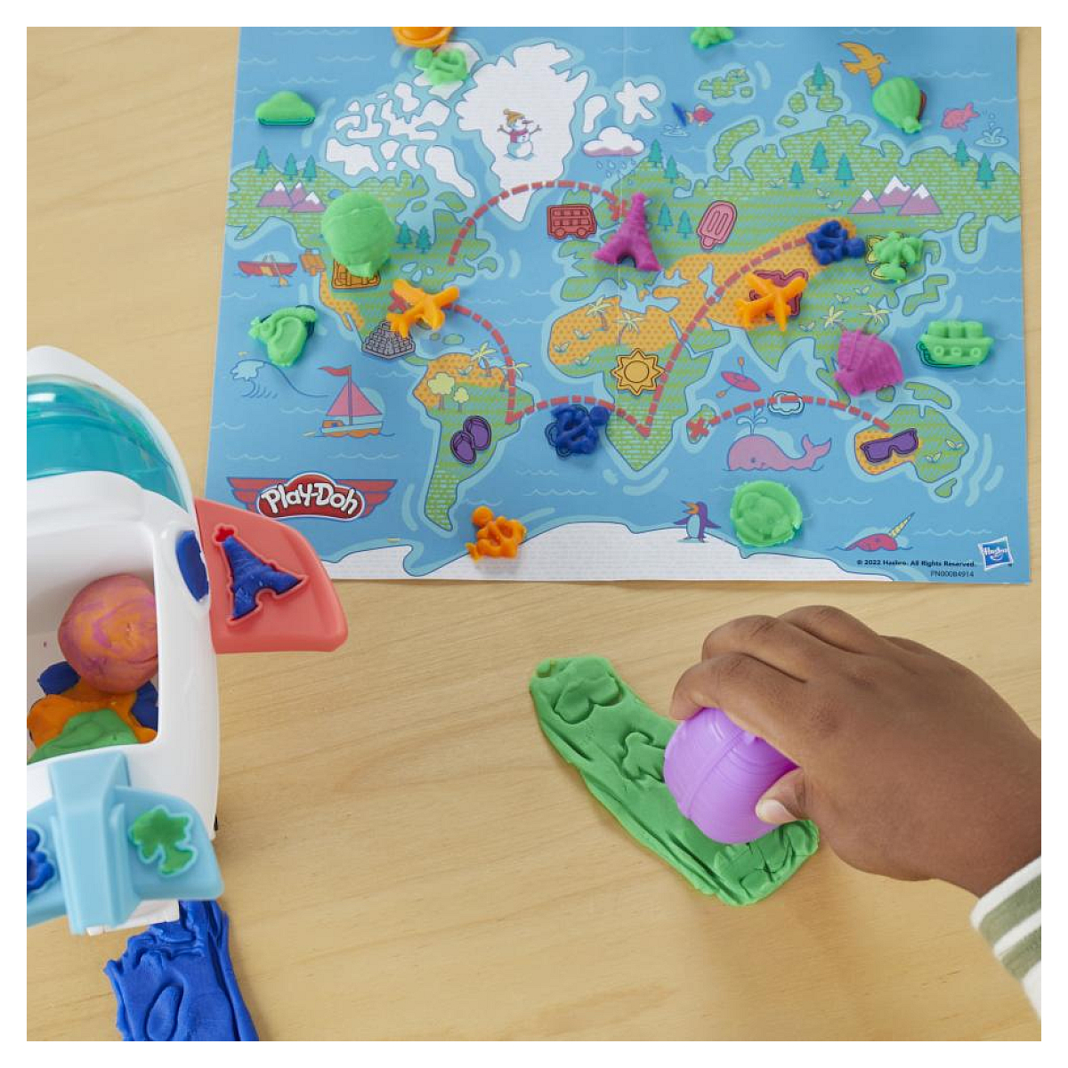 Mapa mundial de Play-Doh con figuras de plastilina de colores. Una mano presiona plastilina morada sobre plastilina verde. Un avión de juguete a la izquierda.