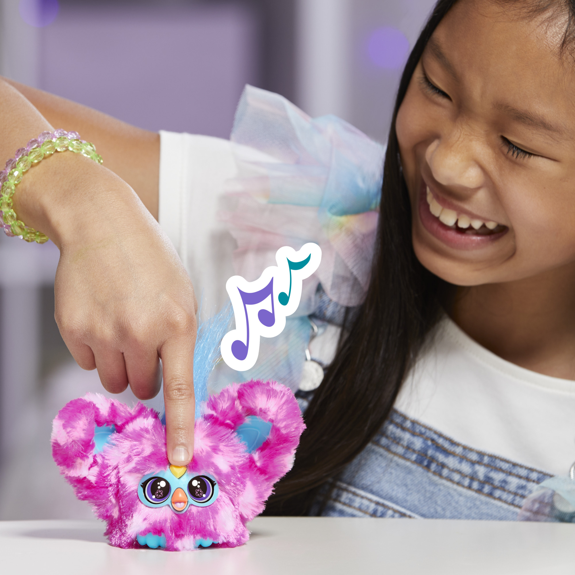 Una niña sonríe mientras toca un juguete rosa. Notas musicales aparecen encima. Lleva una camisa blanca y mezclilla. Una pulsera está en su muñeca.
