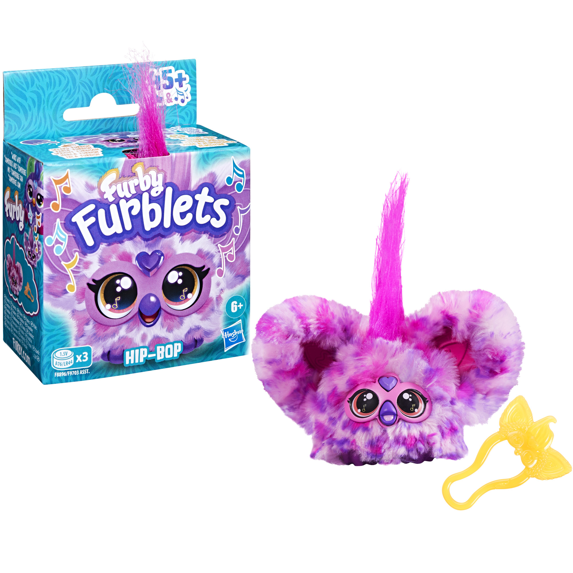 Una caja de juguetes y un juguete Furblets. El juguete es morado y rosa, con ojos grandes. Un accesorio amarillo está al lado.