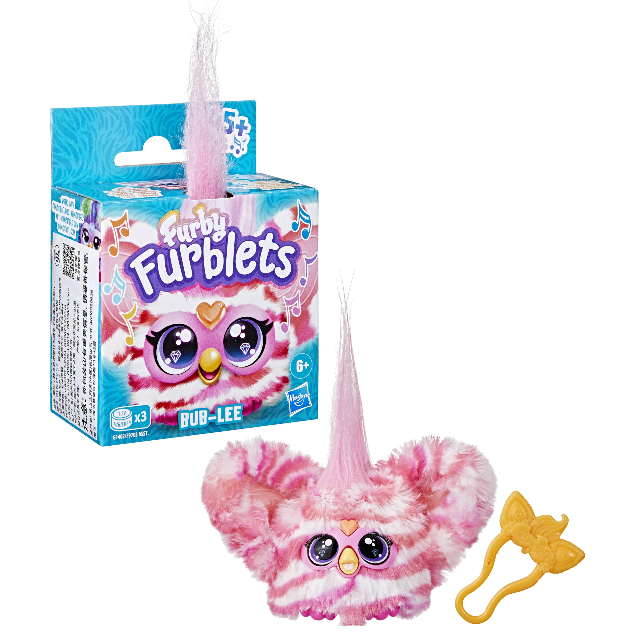 Un juguete Furblets en una caja. Es una criatura de peluche rosa y blanca con ojos grandes, un pico amarillo y un clip amarillo.