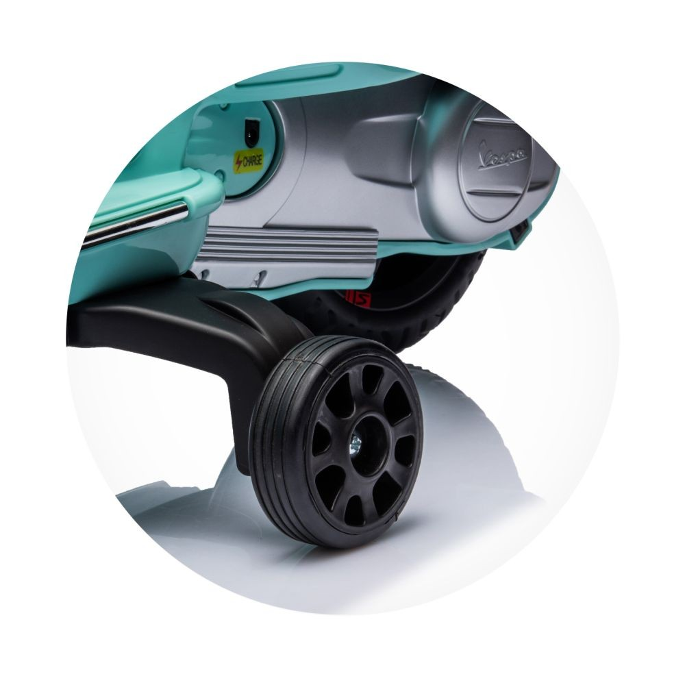 Nahaufnahme eines Spielzeug-Vespa-Rollers. Er ist hellblau mit silbernen Akzenten. Das schwarze Rad steht im Fokus.