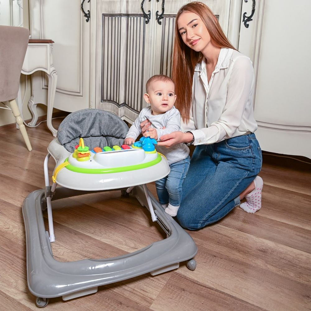 Eine Frau und ein Baby in einem Walker. Die Frau kniet. Das Baby hält das Spielzeug. Holzboden.