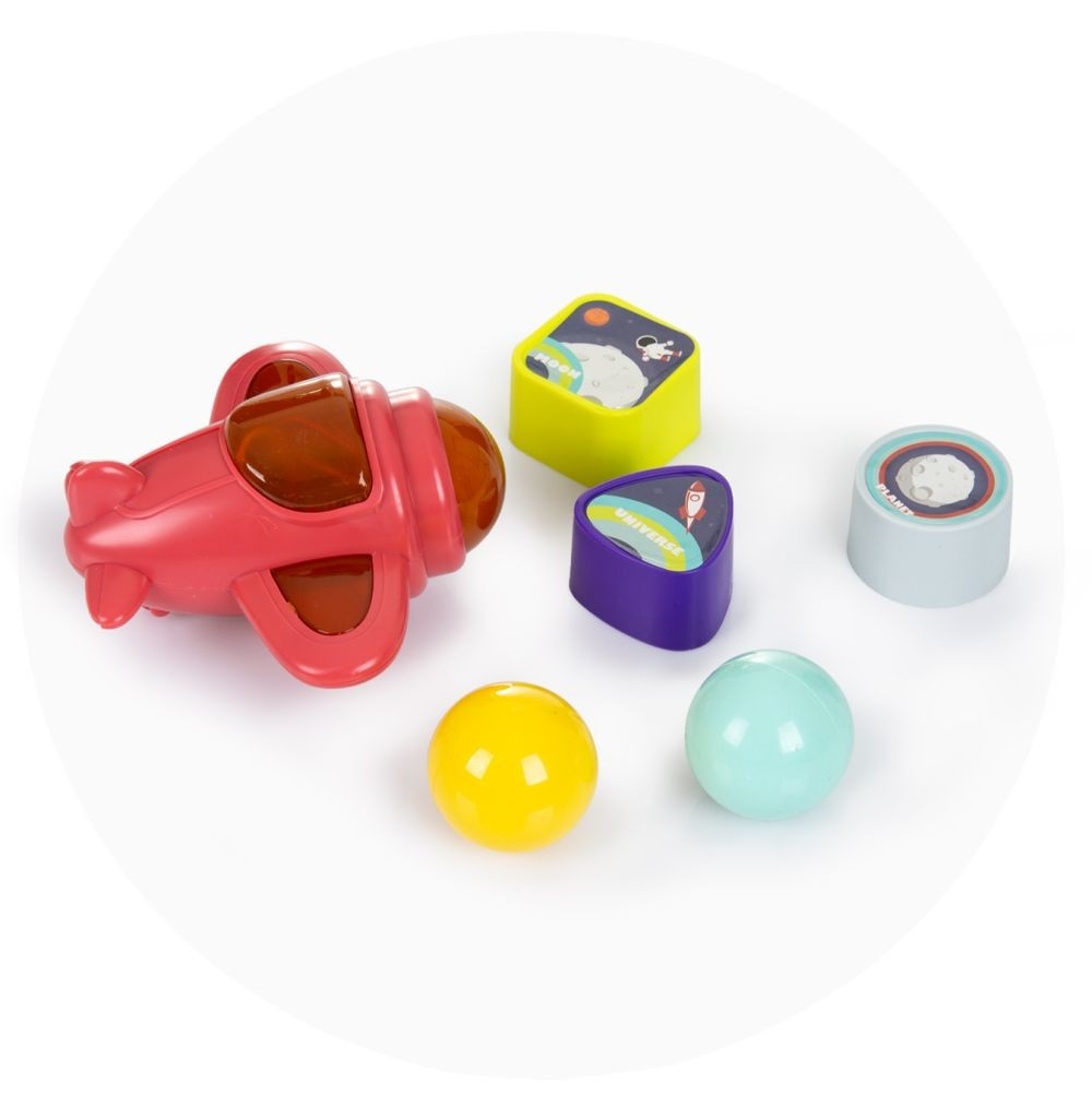 Ein rotes Spielzeugflugzeug, gelbe und blaue Kugeln sowie bunte Blöcke mit Weltraum-Motiven liegen auf einer weißen Oberfläche.